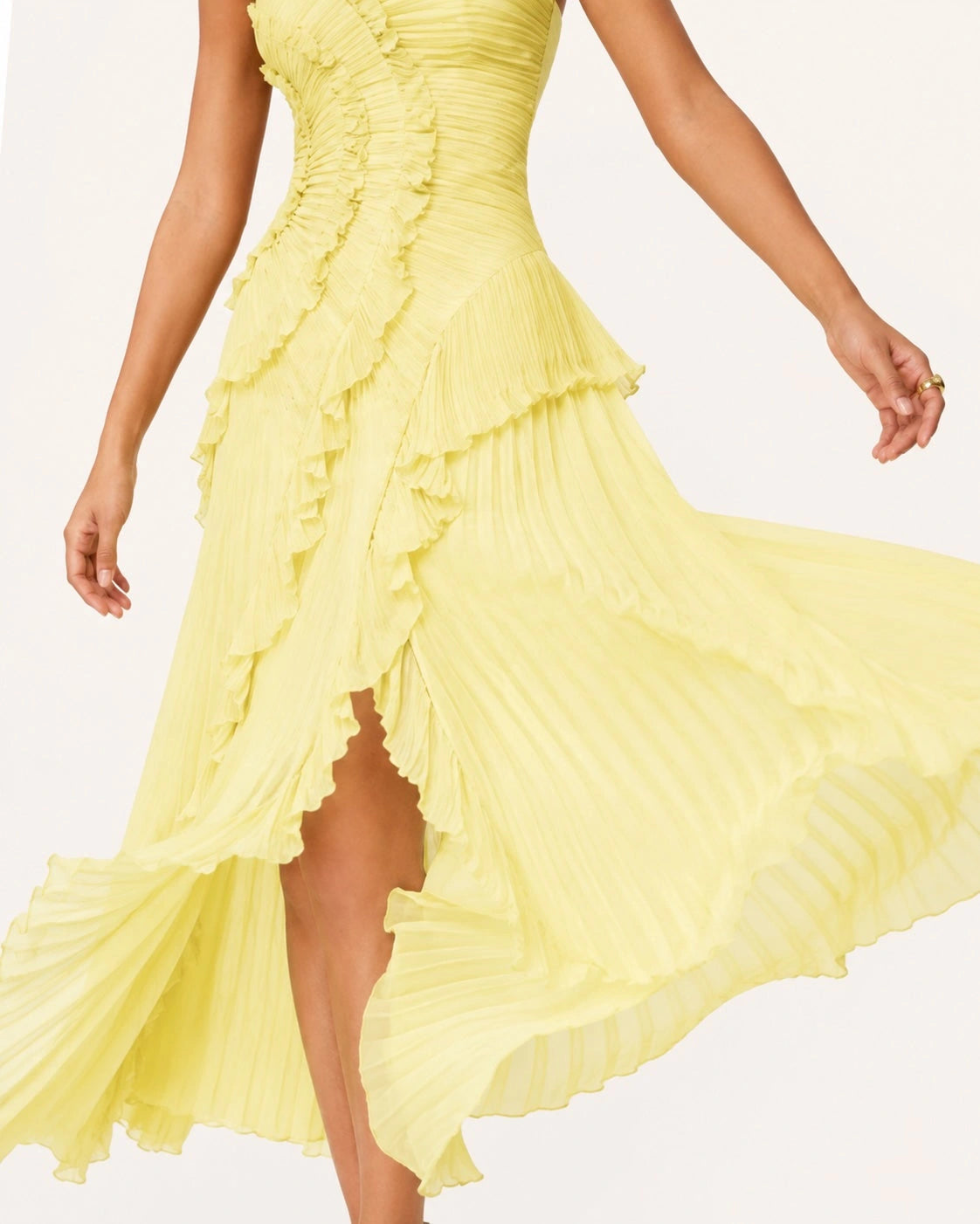 Gros plan sur la jupe asymétrique plissée et les volants en cascade d’une robe jaune pastel, offrant légèreté, fluidité et mouvement naturel.