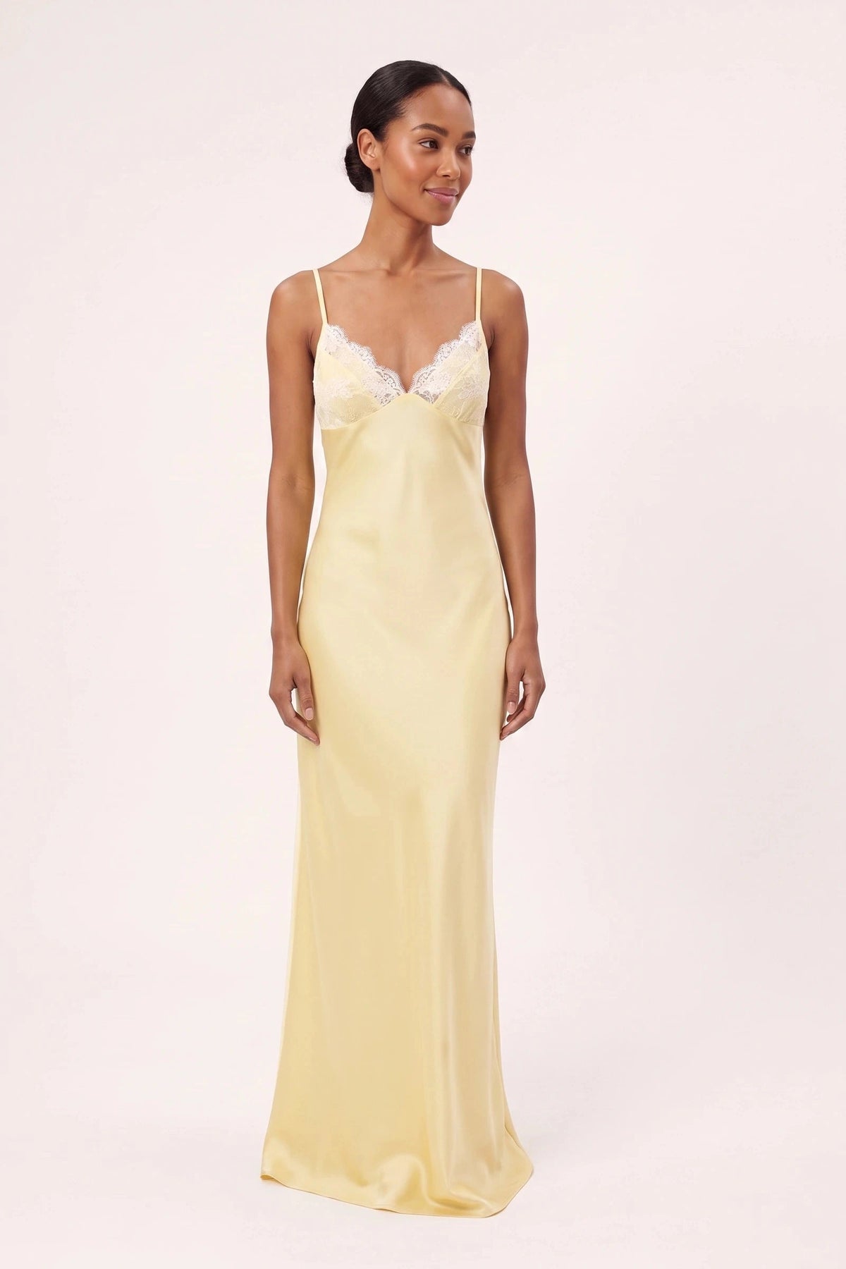Robe satin dentelle dos nu Alyssa jaune portée de face par une mannequin métisse sur fond neutre clair, décolleté V dentelle et coupe longue satinée