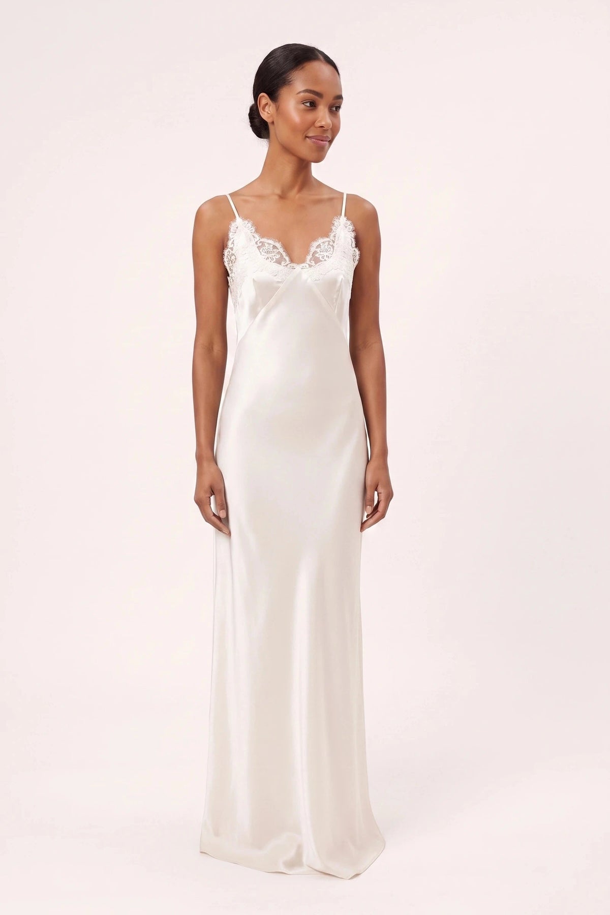 Robe satin dentelle dos nu Alyssa blanche portée de face par une mannequin métisse sur fond neutre clair, dentelle florale fidèle au décolleté V et fines bretelles