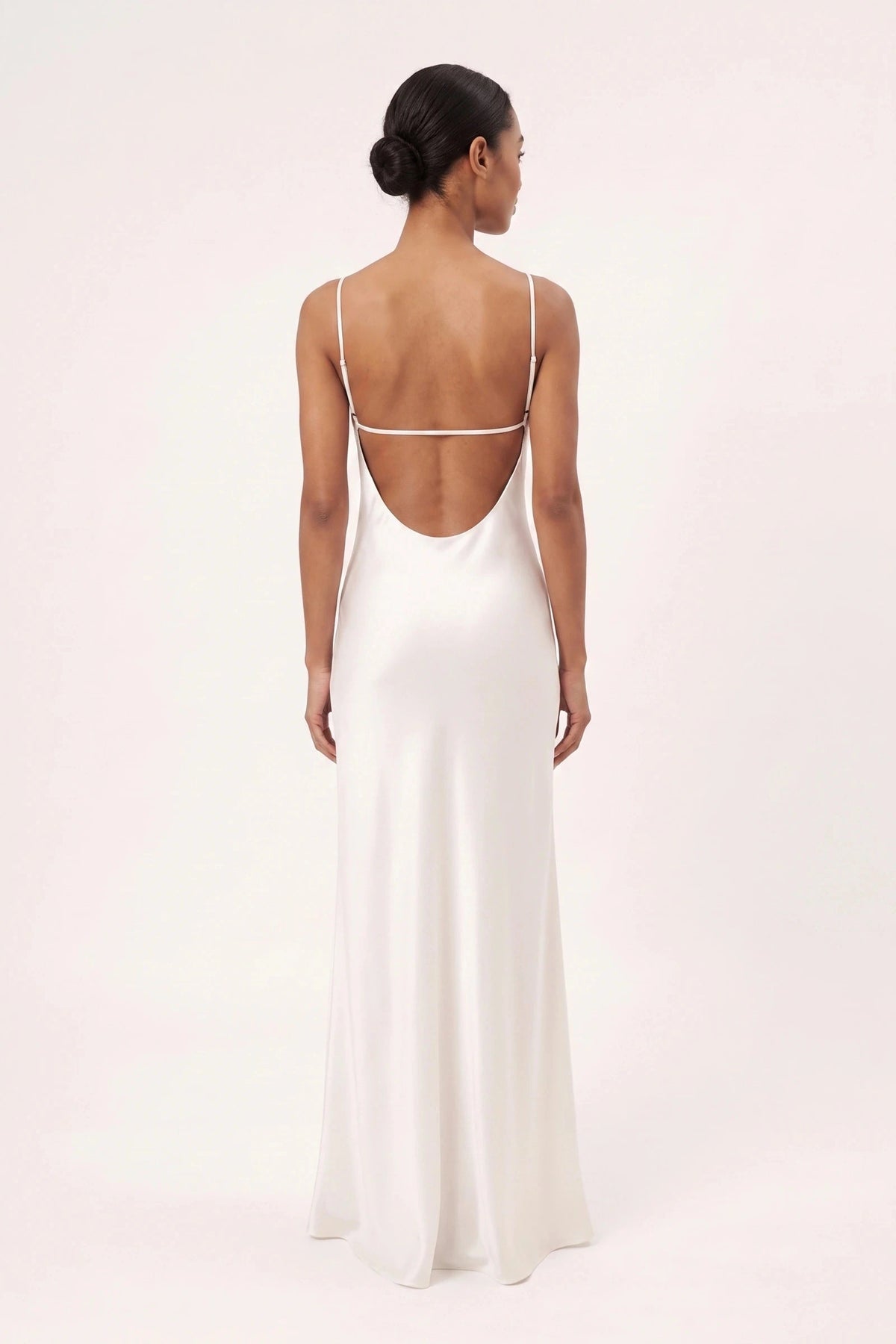 Robe satin dentelle dos nu Alyssa blanche portée de dos par une mannequin métisse sur fond neutre clair, dos nu sans dentelle avec fines bretelles blanches