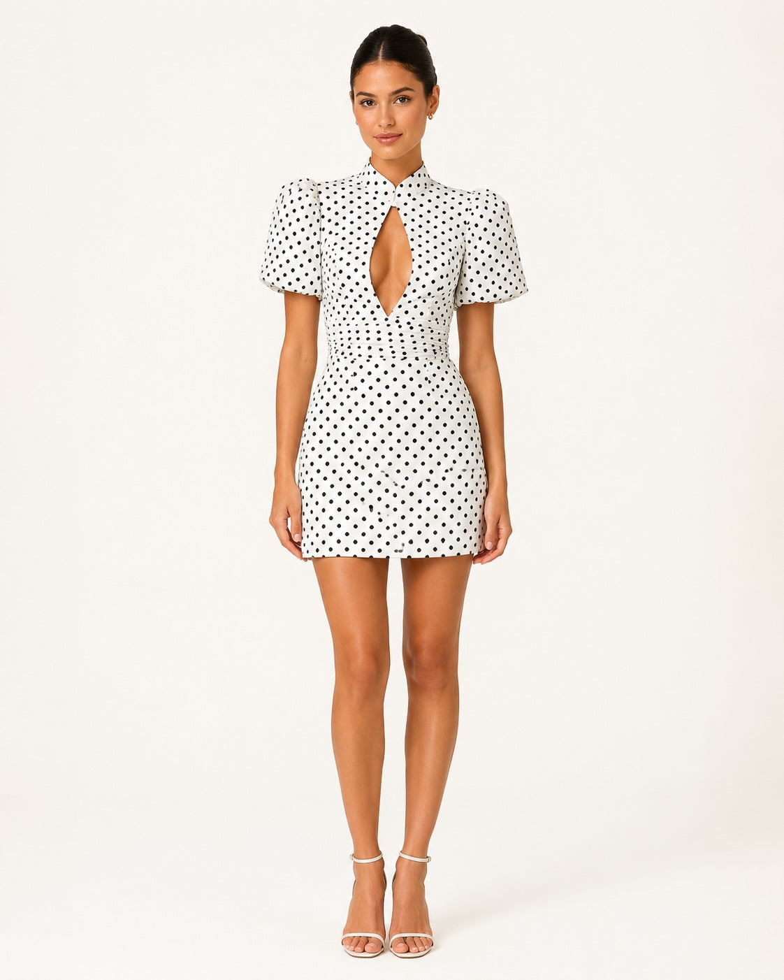 Vue de face de la robe courte Stella blanche à pois noirs, col montant, manches ballon, taille ajustée et décolleté goutte, idéale pour une tenue chic de soirée ou de cocktail.