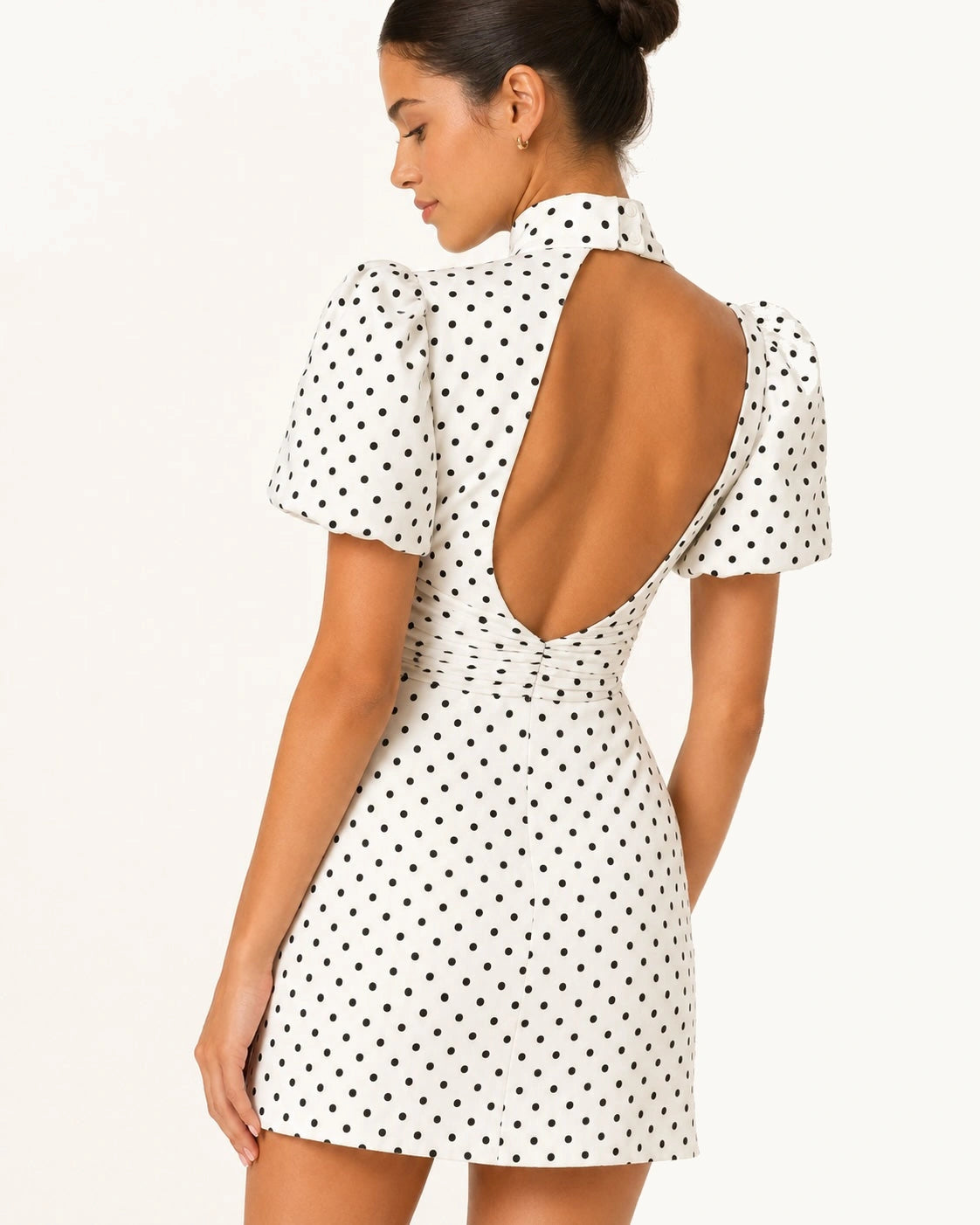 Gros plan du dos ouvert en V de la robe courte blanche Stella à pois noirs, mettant en valeur les finitions, la coupe cintrée et le design féminin du modèle.