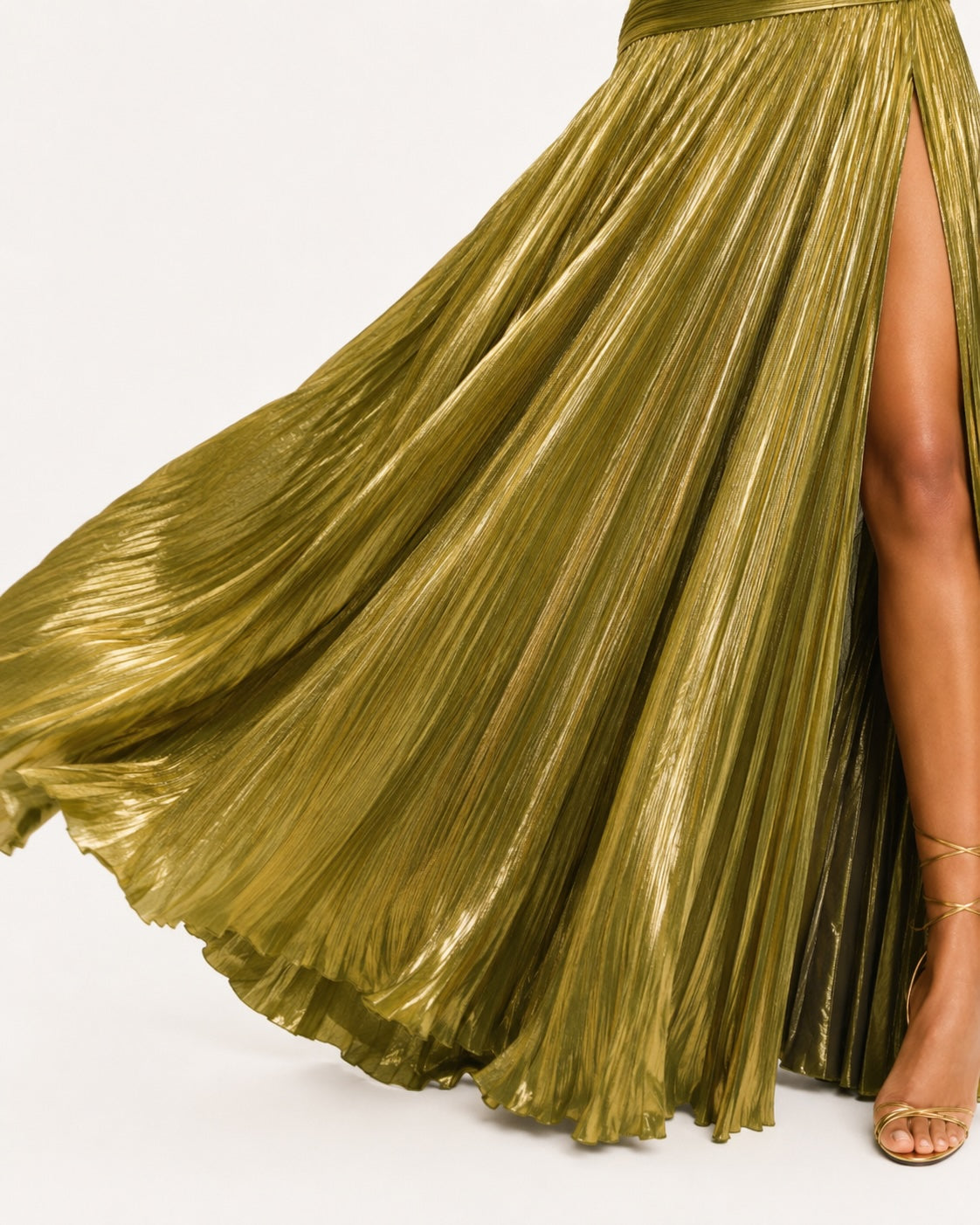 Robe longue plissée dorée avec fente haute et tissu lumineux effet lamé, mettant en valeur un mouvement fluide et élégant pour une tenue de soirée glamour.