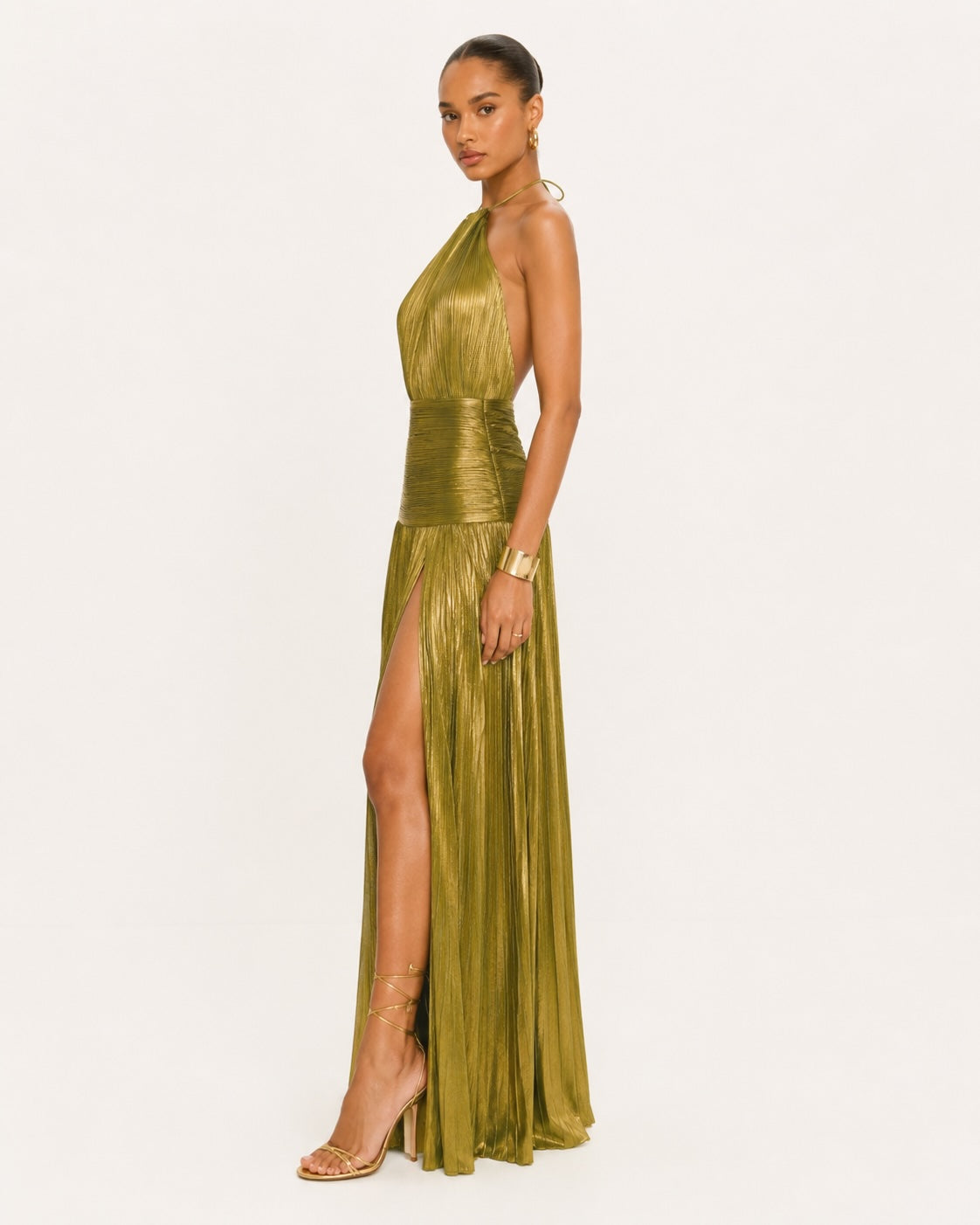 Silhouette de profil d’une robe maxi dorée plissée à col montant, mettant en avant la coupe fluide, la fente sensuelle et l’élégance contemporaine.