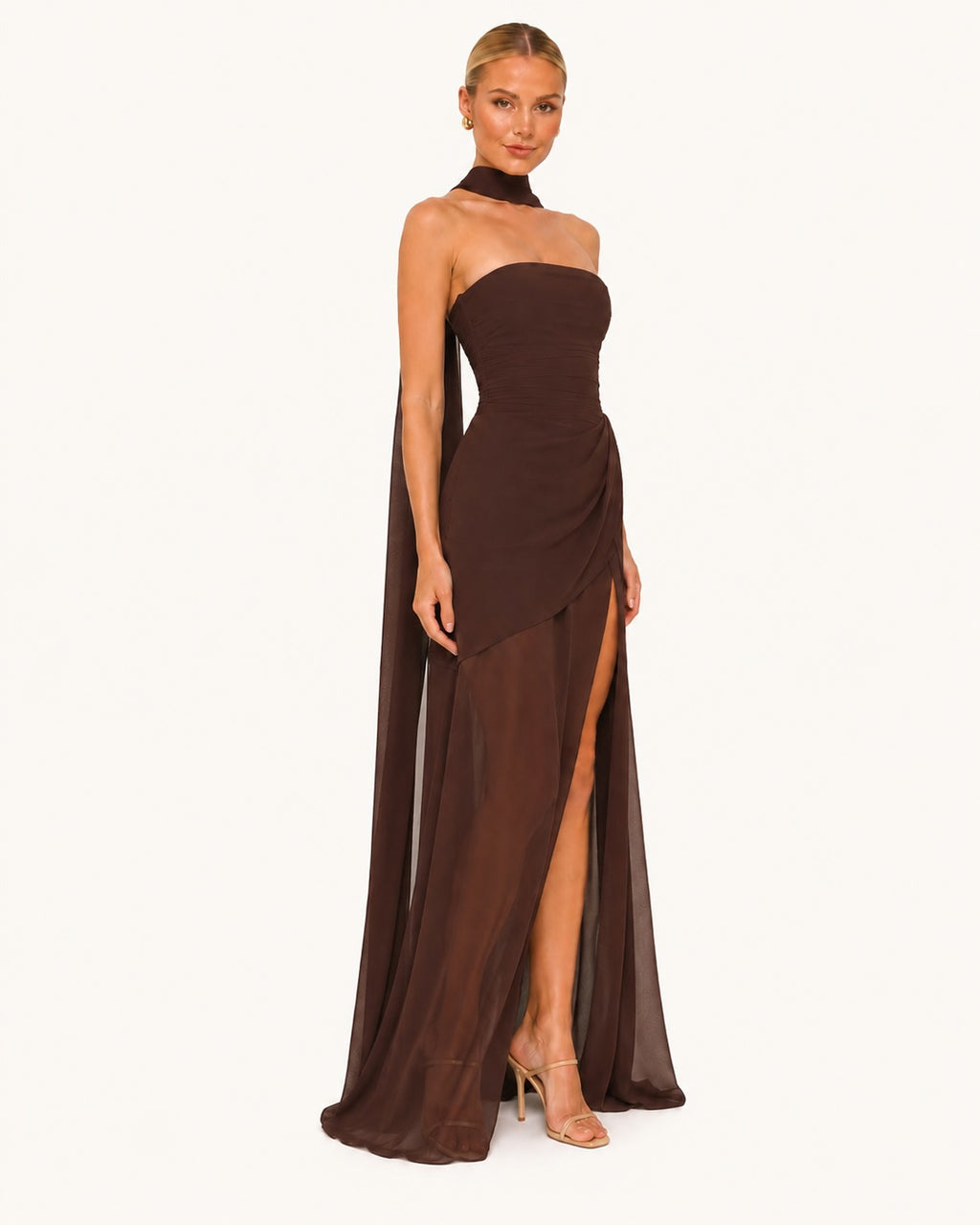 Robe longue marron chocolat asymétrique avec bustier drapé, fente élégante sur la jambe et voile fluide, idéale pour une soirée chic ou une cérémonie raffinée. Vue trois quarts.