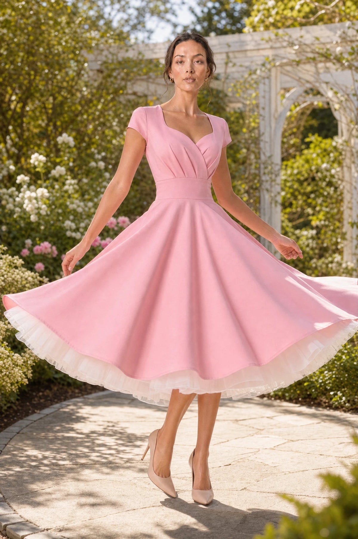Jupon crinoline blanc porté sous la robe vintage rose pin-up Odette par Nath en tourbillon dans un jardin ensoleillé, effet de volume visible avec le tulle blanc qui dépasse sous l'ourlet de la jupe en corolle Image