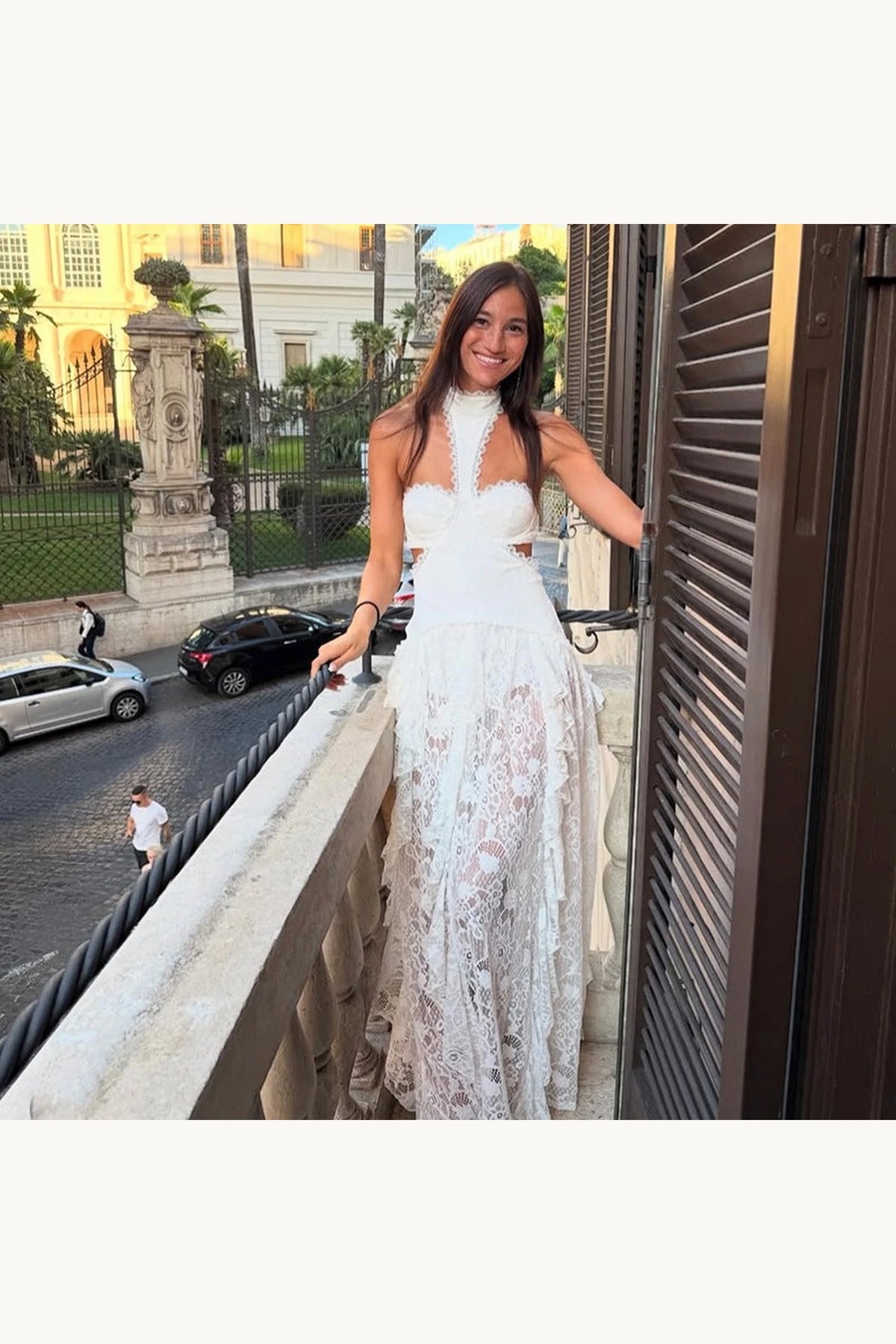 Robe bohème blanche dentelle Sienna portée sur balcon, vue face, bustier féminin, découpes latérales et jupe longue transparente