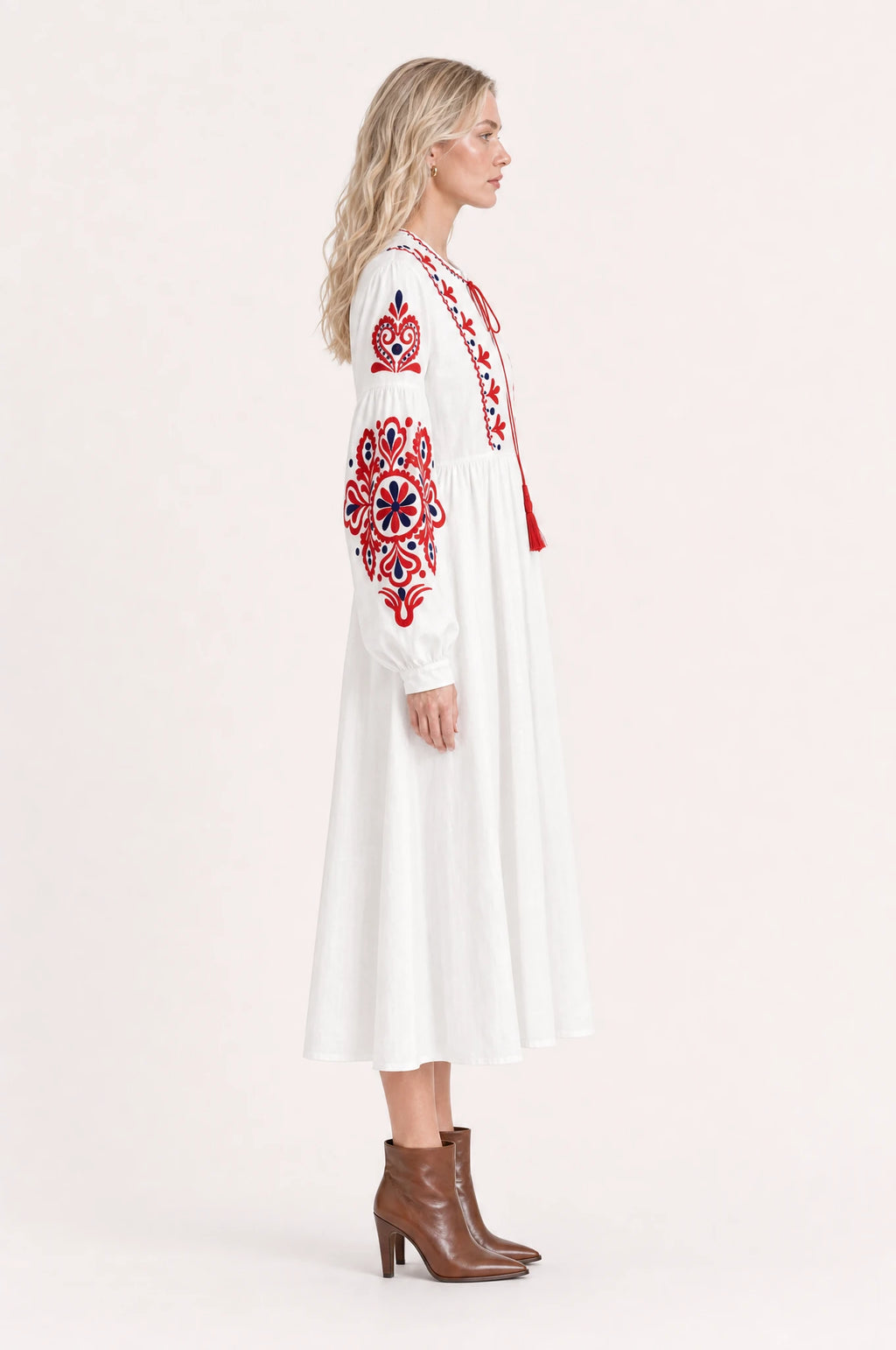 Robe bohème brodée blanche Faustine vue de profil portée par Sophie cheveux détachés, silhouette évasée taille haute, jupe plissée jusqu'à mi-mollet, bottines en cuir marron