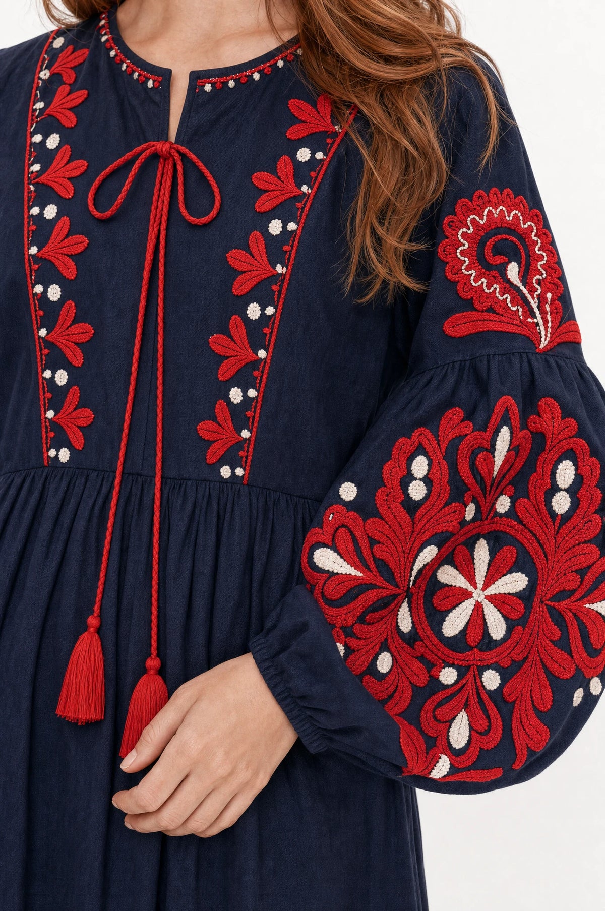 Gros plan sur la broderie florale rouge et blanche et le lien à pompons de la robe bohème brodée bleu marine Constance, détail des manches bouffantes et du tissu coton