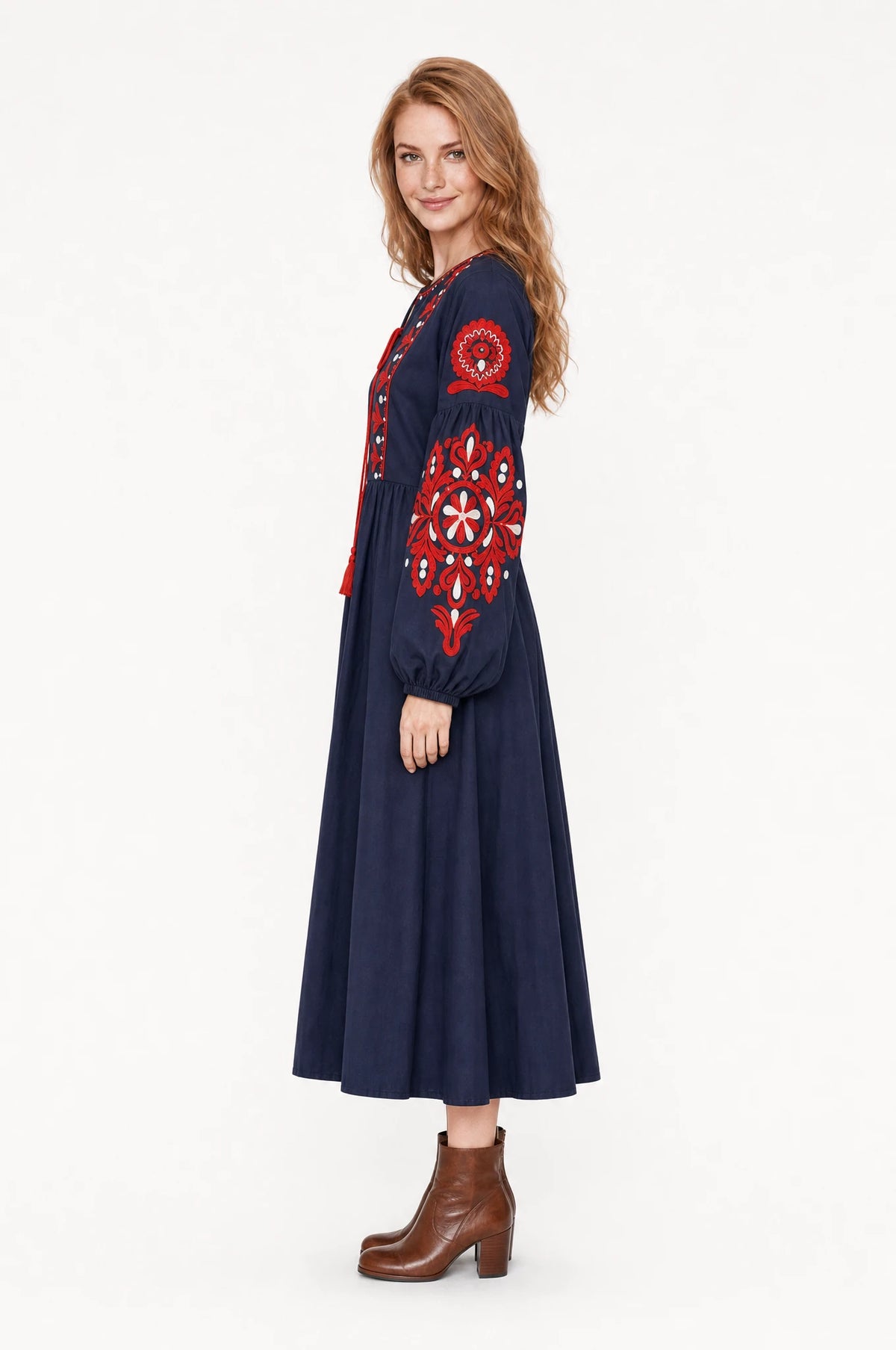 Robe bohème brodée bleu marine Constance vue de profil portée par Julie cheveux détachés, silhouette évasée taille haute, jupe plissée jusqu'à mi-mollet, bottines en cuir marron