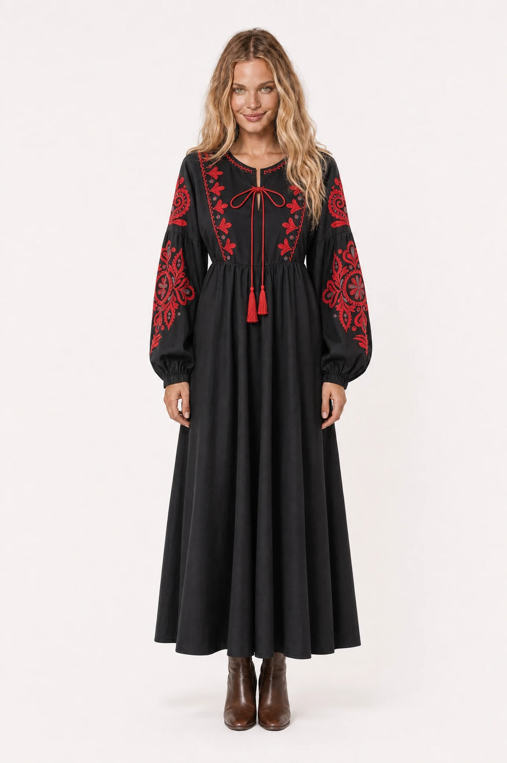 Robe bohème brodée noire Agathe portée de face par Aude cheveux détachés, col rond à lien pompons rouges, broderie florale rouge sur l'empiècement et les manches, manches longues bouffantes, bottines en cuir marron