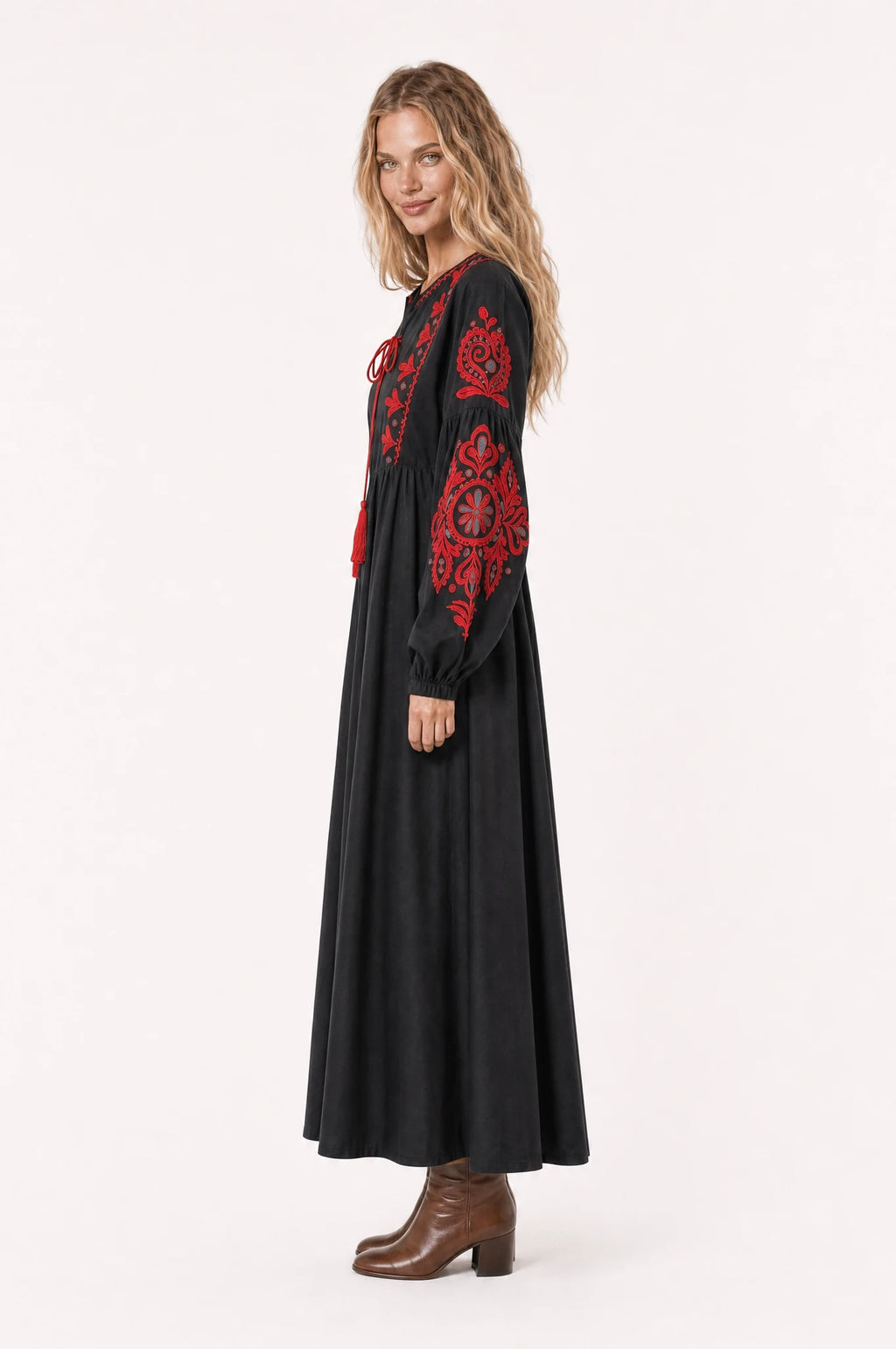 Robe bohème brodée noire Agathe vue de profil portée par Aude cheveux détachés, silhouette évasée taille haute, jupe plissée jusqu'à mi-mollet, bottines en cuir marron