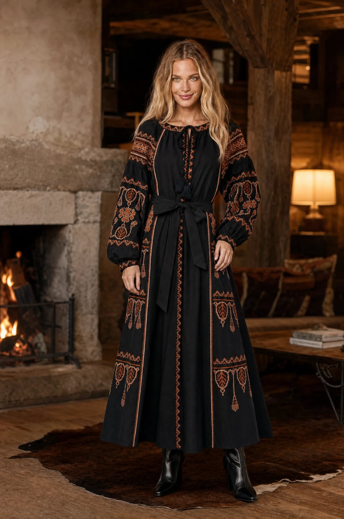 Robe bohème brodée noire Salomé portée par Aude dans un intérieur cosy en hiver, cheminée allumée, poutres apparentes, lumière chaude ambrée, ambiance chaleureuse de soirée d'hiver, bottines noires Image