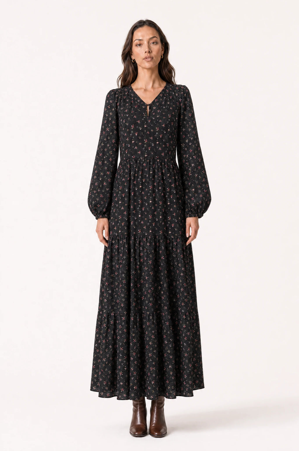 Robe bohème manche longue fleurie noire Pauline portée de face par Nath cheveux détachés, col en V pointu avec bouton keyhole, manches longues bouffantes, taille marquée, jupe évasée à volants, bottines en cuir marron
