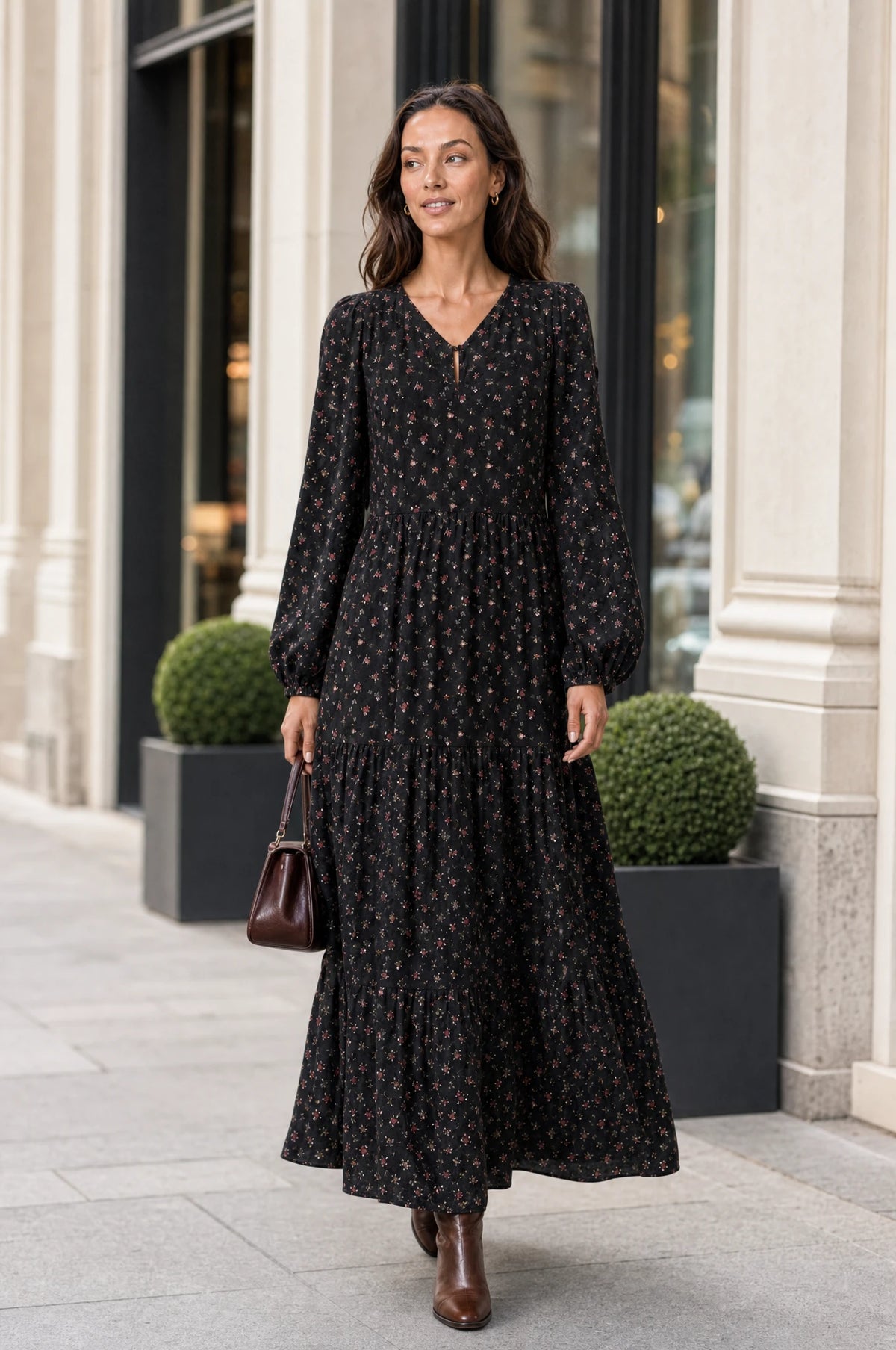 Robe bohème manche longue fleurie noire Pauline portée par Nath dans une rue chic en journée, sac à main en cuir marron, bottines marron, ambiance urbaine élégante
