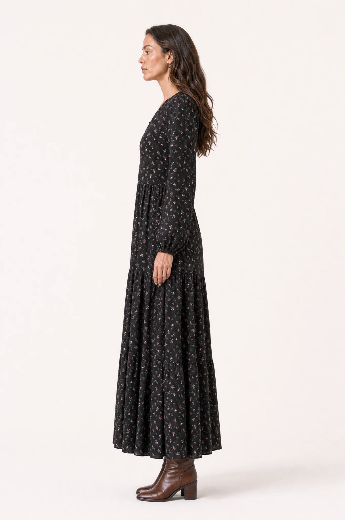 Robe bohème manche longue fleurie noire Pauline vue de profil portée par Nath cheveux détachés, silhouette évasée, jupe longue jusqu'à la cheville, bottines en cuir marron
