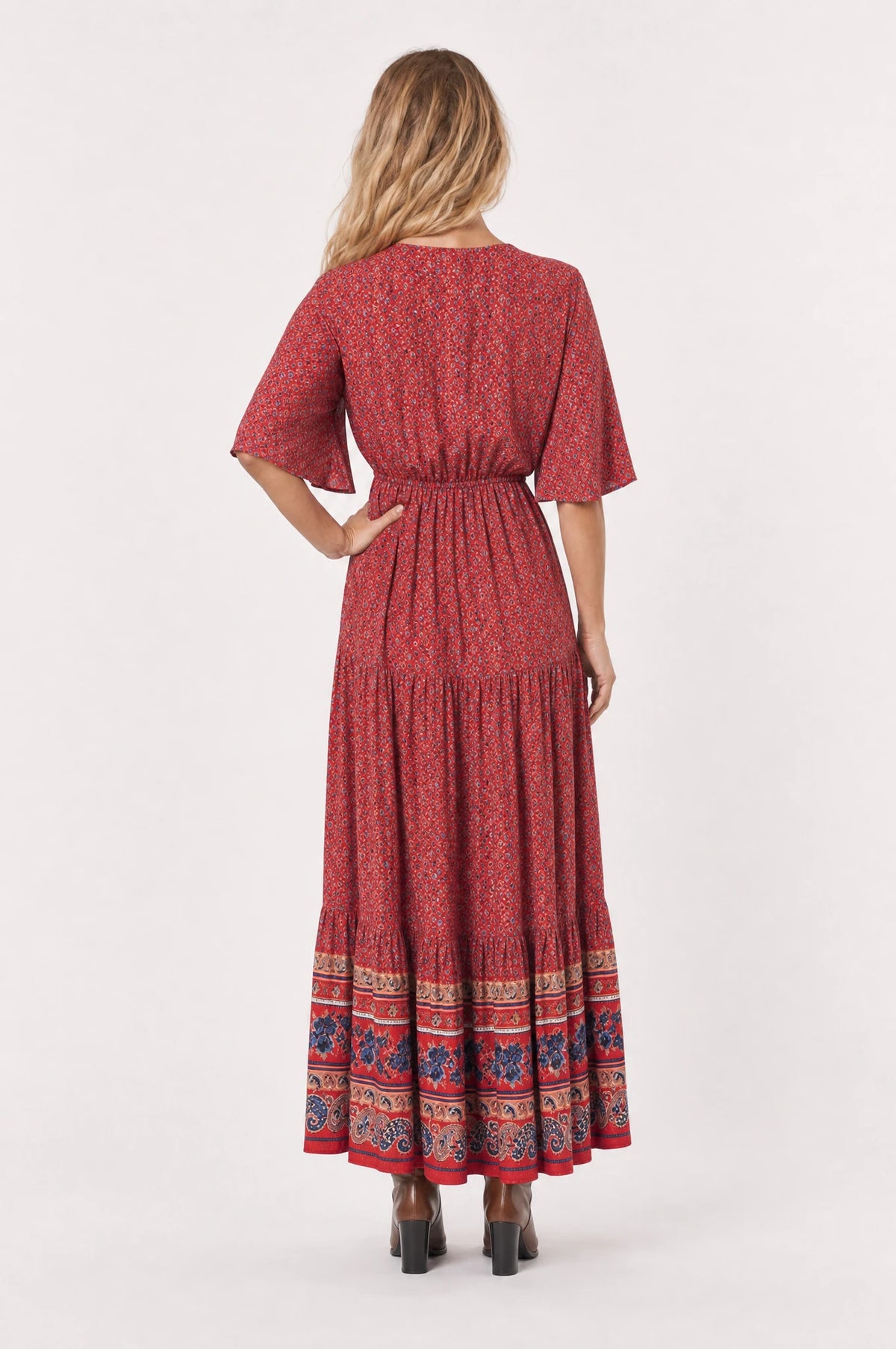 Robe bohème longue fleurie rouge Marguerite portée de dos par Aude, taille élastiquée visible dans le dos, manches courtes évasées, jupe évasée fluide imprimé fleuri jusqu'à la cheville