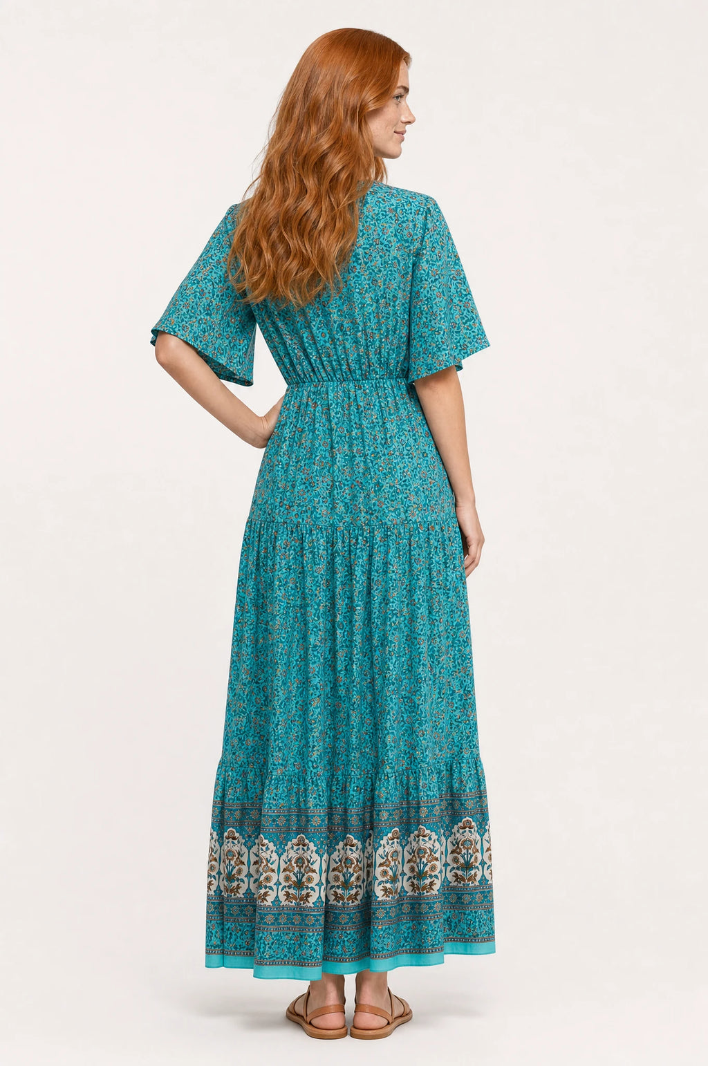 Robe bohème longue fleurie turquoise Céleste portée de dos par Julie, taille élastiquée visible dans le dos, manches courtes évasées, jupe évasée fluide imprimé fleuri jusqu'à la cheville