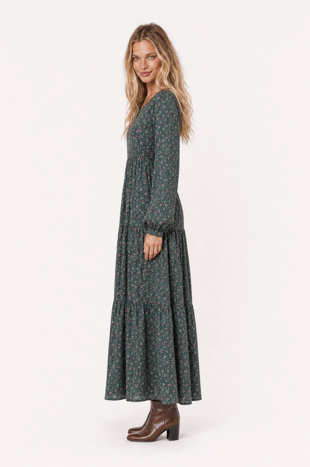 Robe bohème champêtre fleurie verte Roxane vue de profil portée par Aude cheveux détachés, silhouette évasée, jupe longue jusqu'à la cheville, bottines en cuir marron