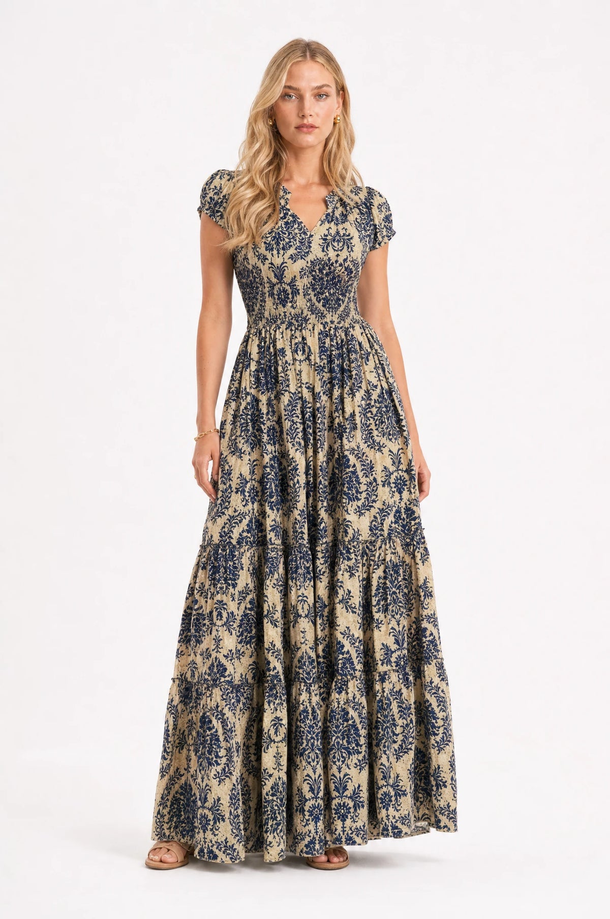 Robe bohème longue fleurie bleu profond Océane portée de face par Sophie cheveux détachés, décolleté en V, bustier froncé smocké, manches courtes légèrement bouffantes, jupe évasée à volants imprimé floral bleu et doré, tenue idéale pour l'été