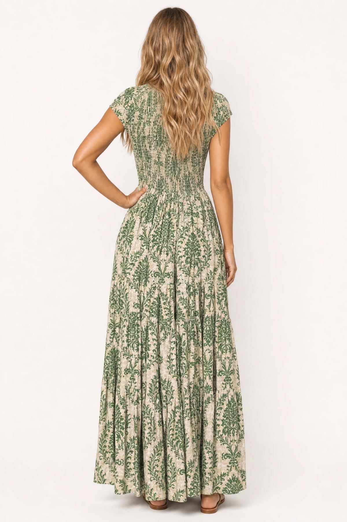 Robe bohème longue fleurie Capucine portée de dos par Aude, bustier smocké continuant sur toute la largeur du dos, jupe évasée à volants imprimé floral vert, coupe fluide et confortable