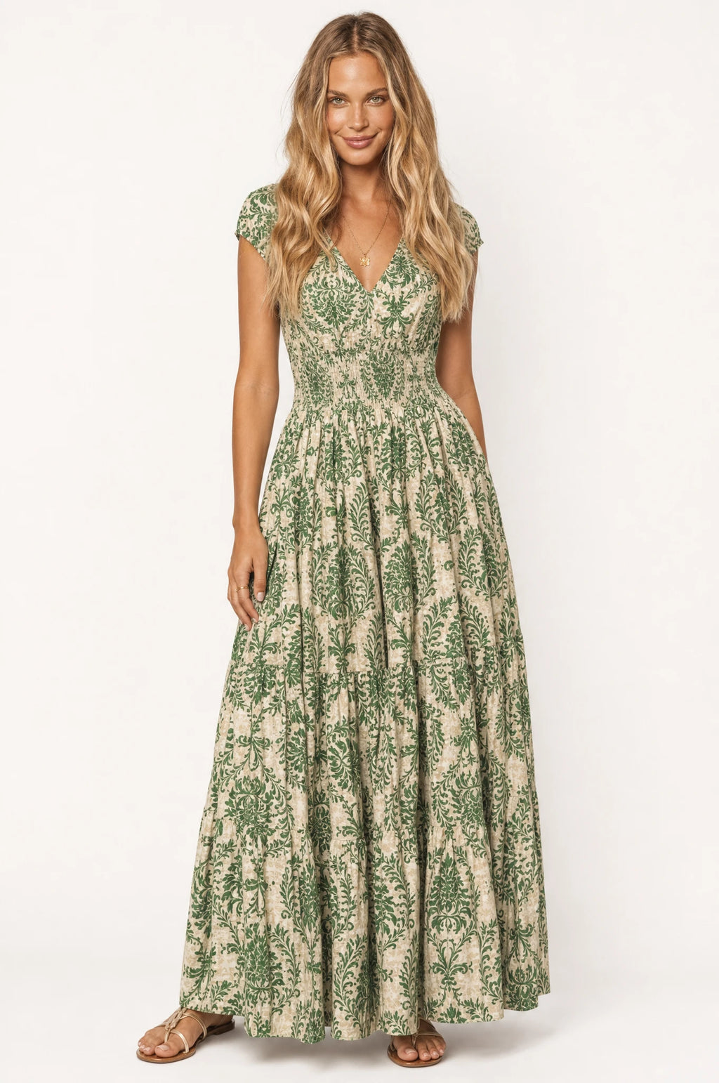 Robe bohème longue fleurie vert Capucine portée de face par Aude, décolleté en V, bustier froncé smocké, manches courtes légèrement bouffantes, jupe évasée à volants imprimé floral vert et écru, tenue idéale pour l'été et les vacances