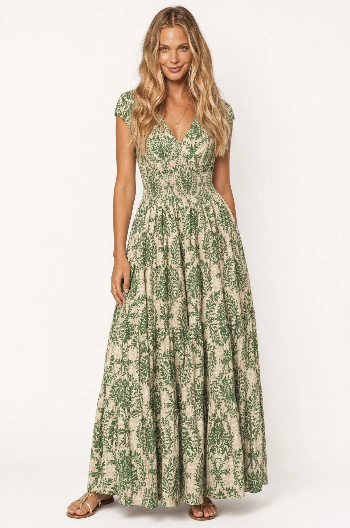 Robe bohème longue fleurie vert Capucine portée de face par Aude, décolleté en V, bustier froncé smocké, manches courtes légèrement bouffantes, jupe évasée à volants imprimé floral vert et écru, tenue idéale pour l'été et les vacances