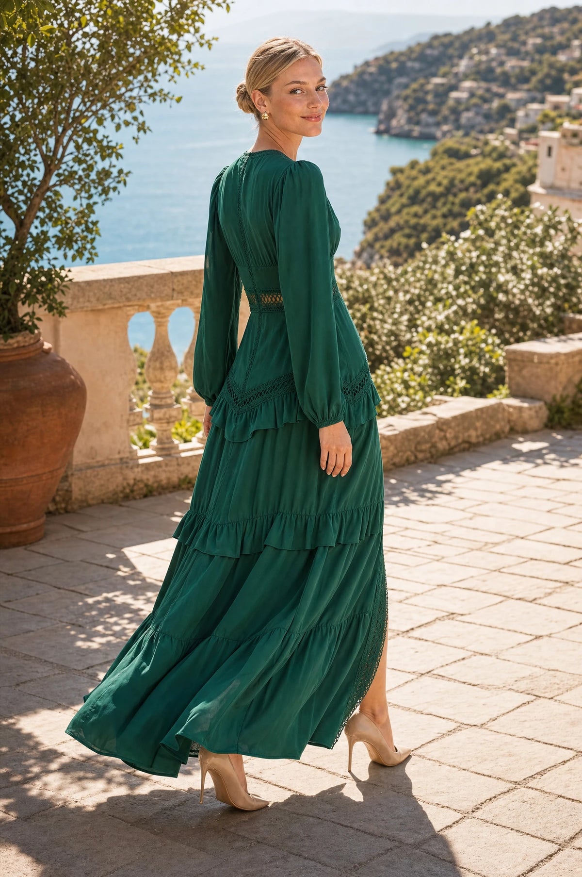 Robe bohème longue verte Ondine portée par Sophie en marche sur une terrasse en pierre surplombant la mer Méditerranée, mains libres, regard par-dessus l'épaule, ambiance ensoleillée
