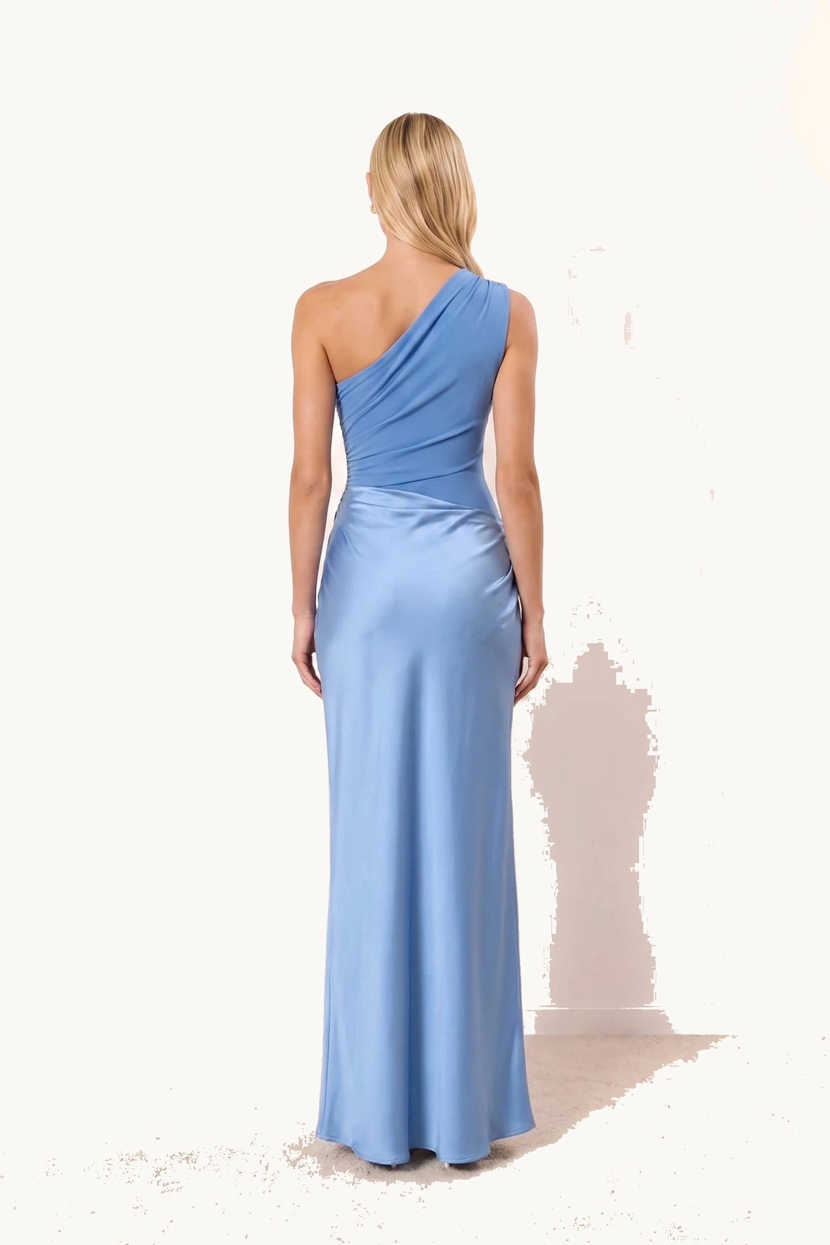 Robe chic longue Jade bleue portée de dos par le mannequin Chloé sur fond neutre clair, haut asymétrique plus foncé et jupe bleu clair satinée