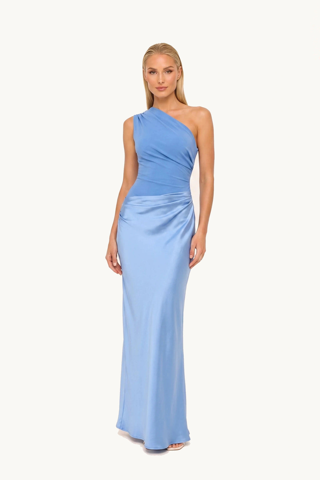 Robe chic longue Jade bleue portée de face par le mannequin Chloé sur fond neutre clair, haut bleu plus foncé mat, jupe bleu clair satinée, épaule asymétrique et drapé fournisseur