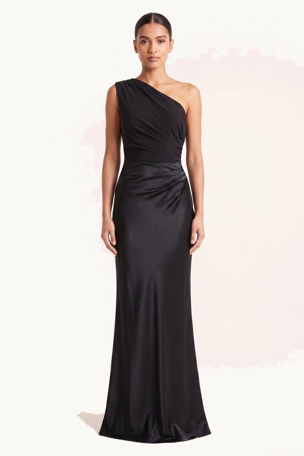 Robe chic longue Jade noire portée de face sur fond neutre clair, haut et jupe en même satin noir, épaule asymétrique, drapé à la taille et allure cérémonie
