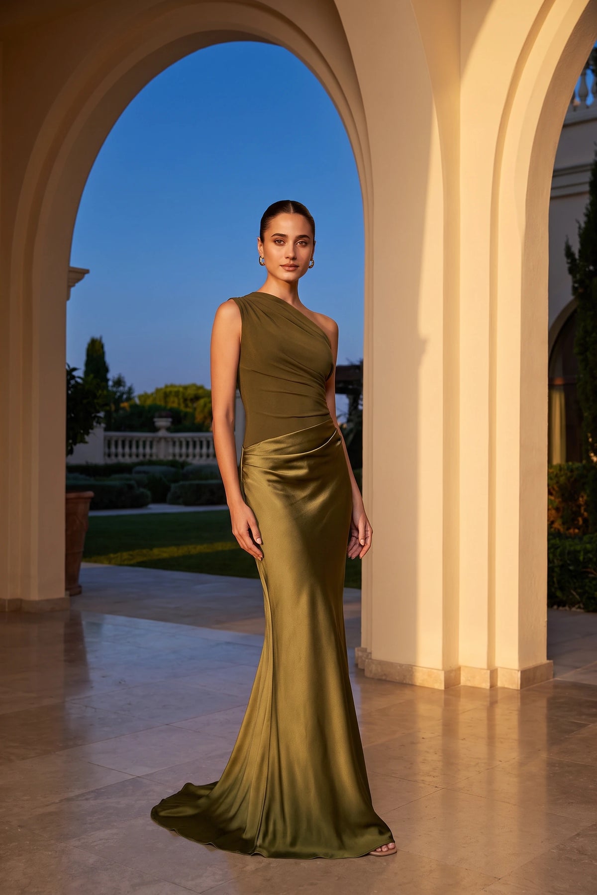 Robe chic longue Jade vert olive portée sous des arches lumineuses, épaule asymétrique, drapé satiné et style cérémonie