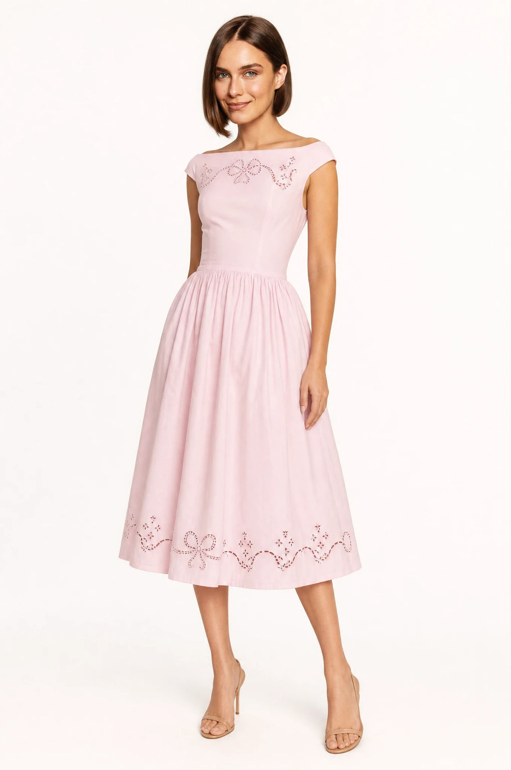 Robe chic rose brodée Anaïs portée de face par Élodie chignon bob châtain, encolure bateau, manches capes, broderie ajourée florale à motifs de nœuds sur l'empiècement, taille cintrée, jupe midi évasée en corolle