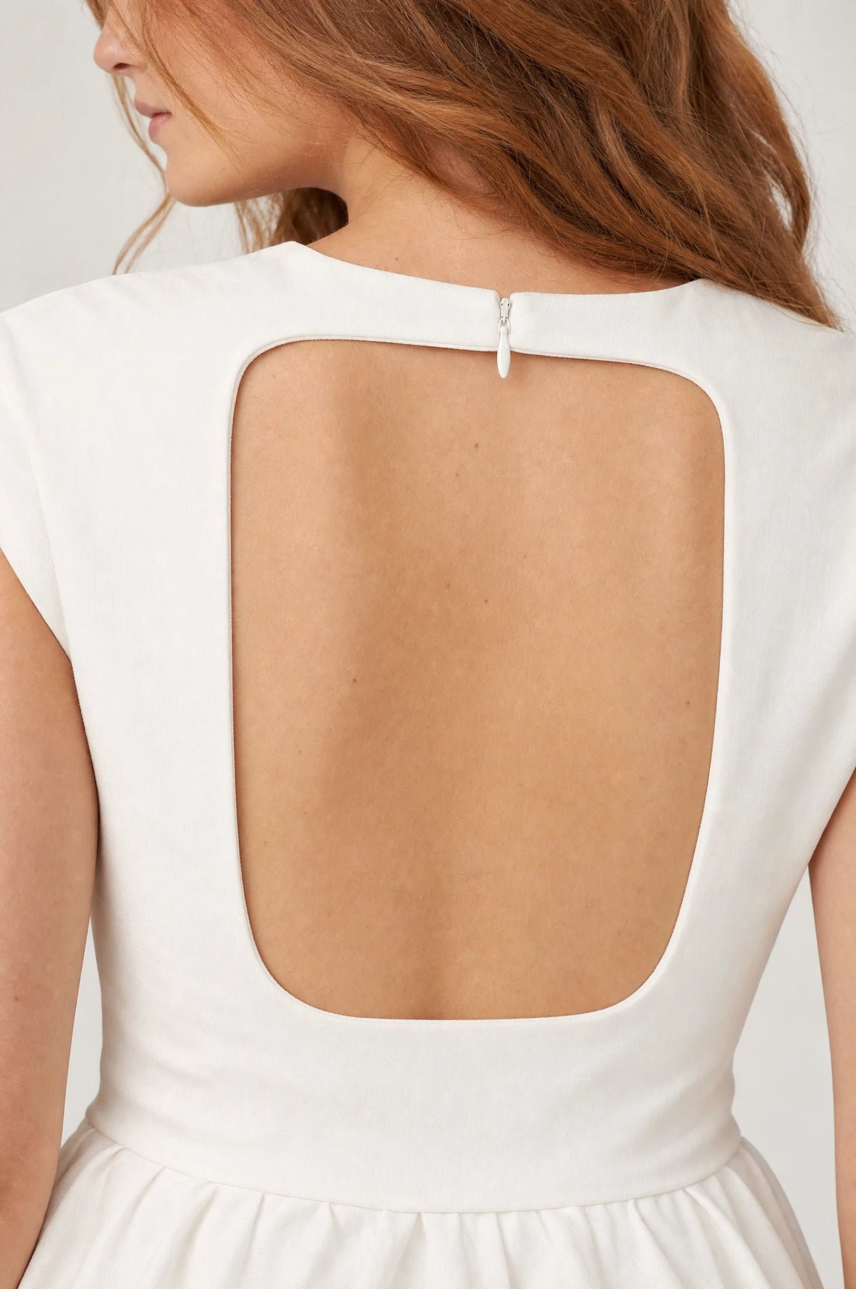 Gros plan sur la découpe carrée à bas arrondi dans le dos de la robe cocktail blanche Charlotte, détail de la fermeture zippée et du tissu structuré