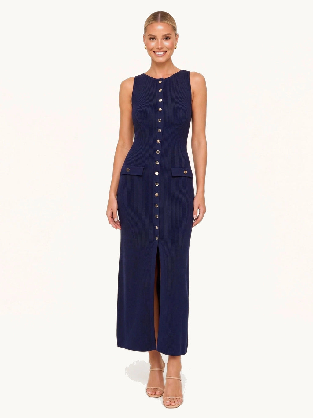 Robe longue en maille bleu marine Lina portée de face par une mannequin blonde souriante sur fond beige ivoire harmonisé fond neutre clair, texture côtelée nette, boutons dorés et fente devant.