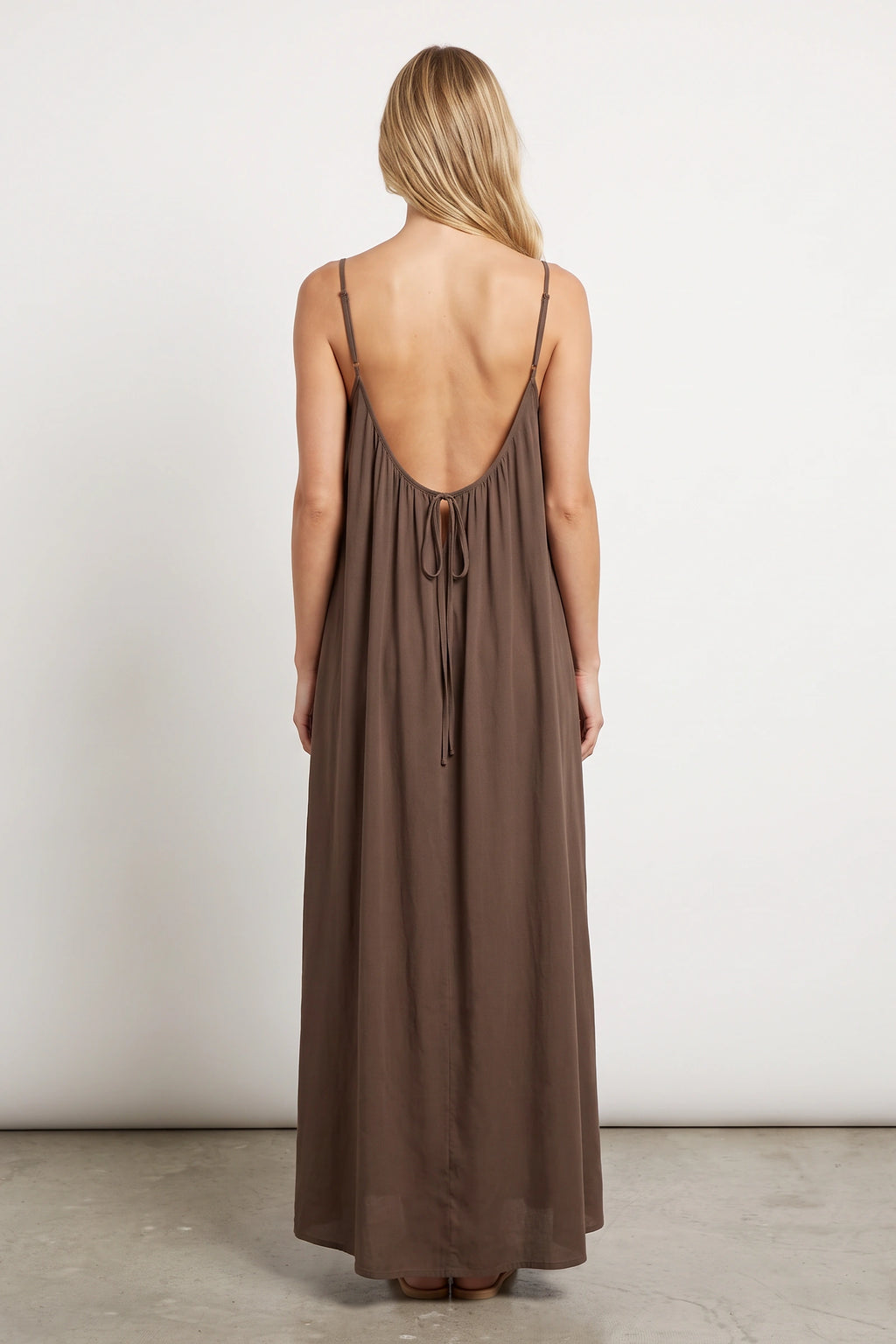 Robe longue casual dos nu Ambre couleur Café portée de dos par Chloé cheveux détachés, fines bretelles, dos ouvert arrondi avec petit détail bas du dos et coupe fluide sur fond clair