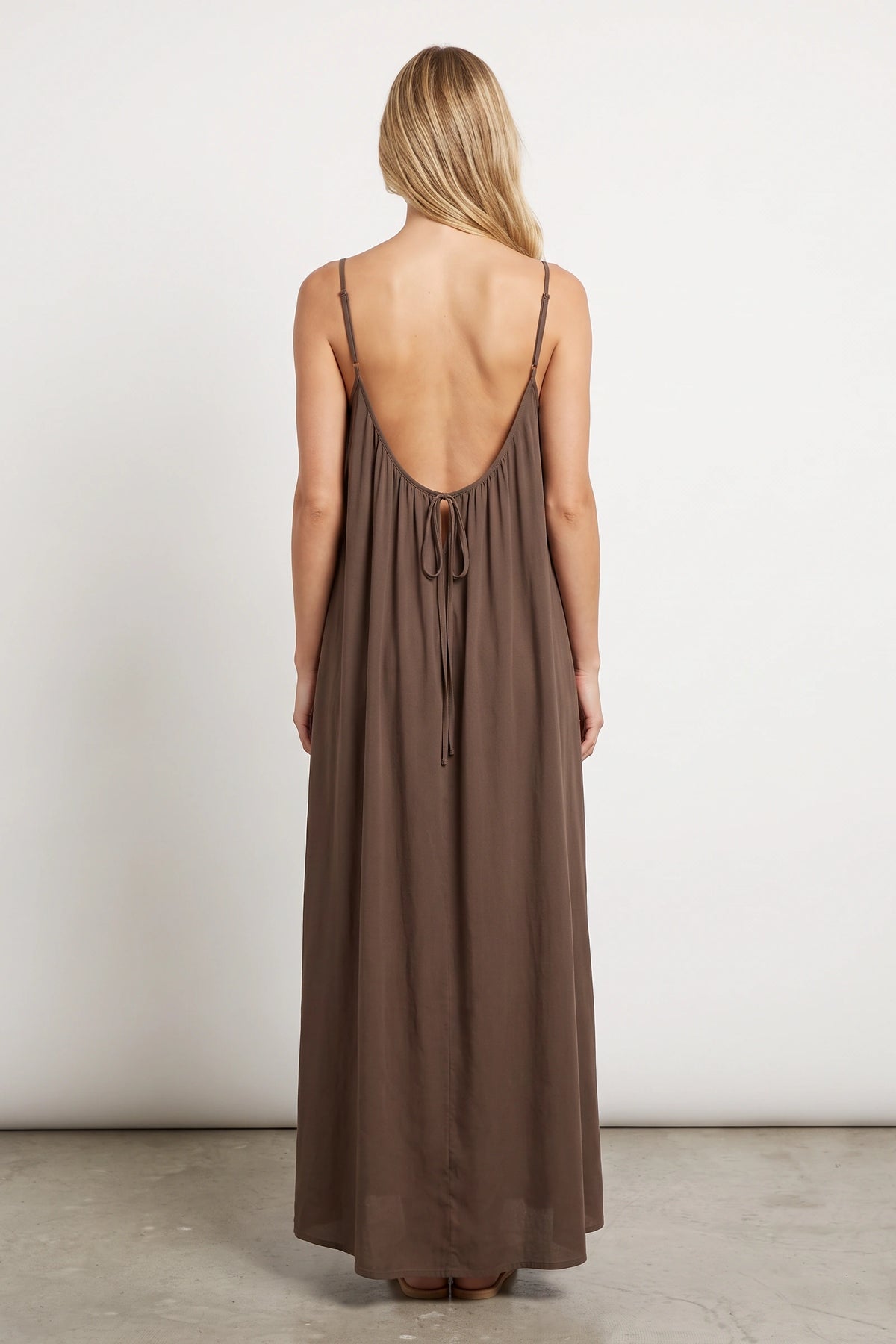 Robe longue casual dos nu Ambre couleur Café portée de dos par Chloé cheveux détachés, fines bretelles, dos ouvert arrondi avec petit détail bas du dos et coupe fluide sur fond clair