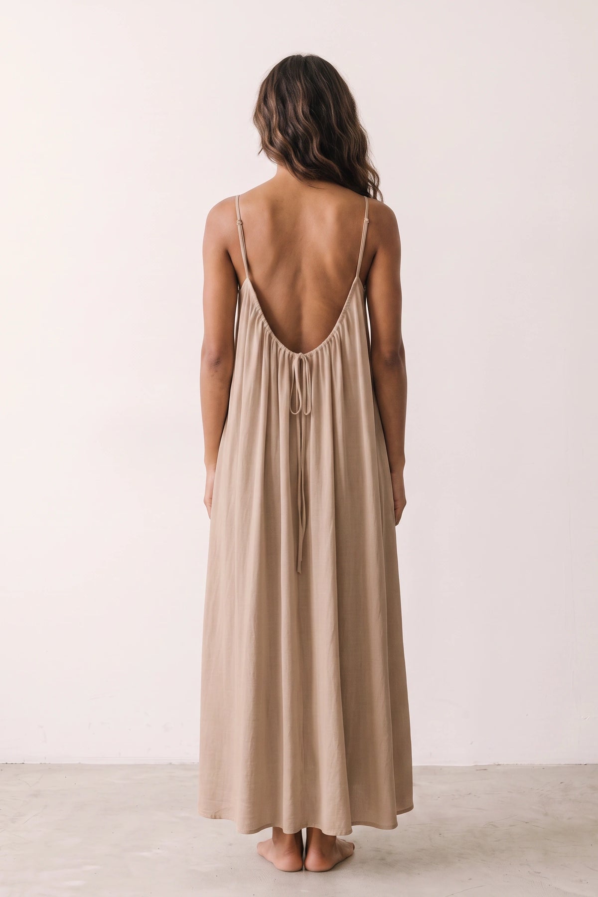 Robe longue casual dos nu Maé couleur Marron clair portée de dos par Camille cheveux détachés, fines bretelles, dos ouvert arrondi avec petit détail bas du dos et coupe fluide sur fond clair