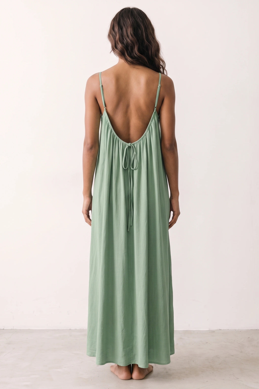Robe longue casual dos nu Maé couleur Vert clair portée de dos par Camille cheveux détachés, fines bretelles, dos ouvert arrondi avec petit détail bas du dos et coupe fluide sur fond clair