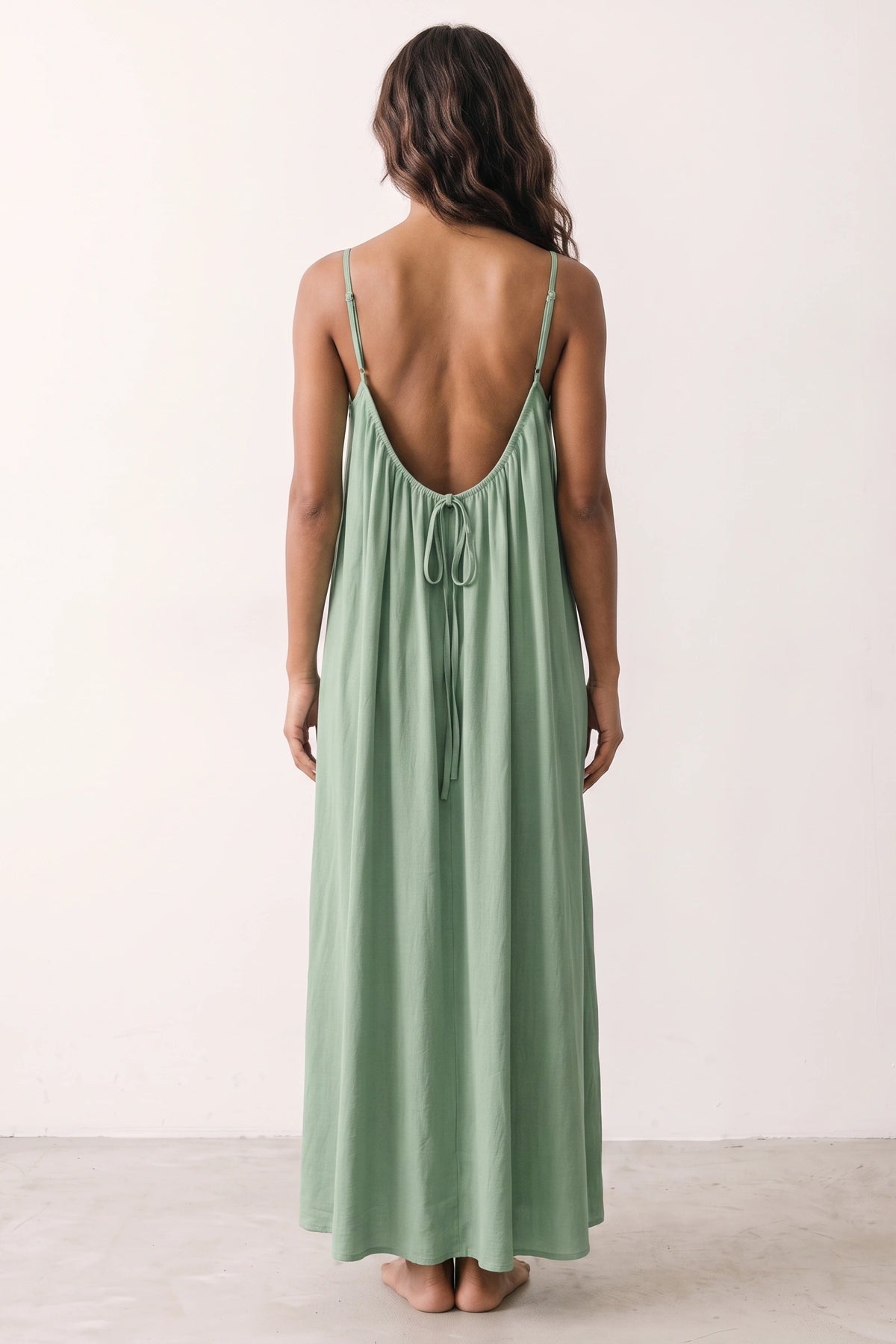 Robe longue casual dos nu Maé couleur Vert clair portée de dos par Camille cheveux détachés, fines bretelles, dos ouvert arrondi avec petit détail bas du dos et coupe fluide sur fond clair