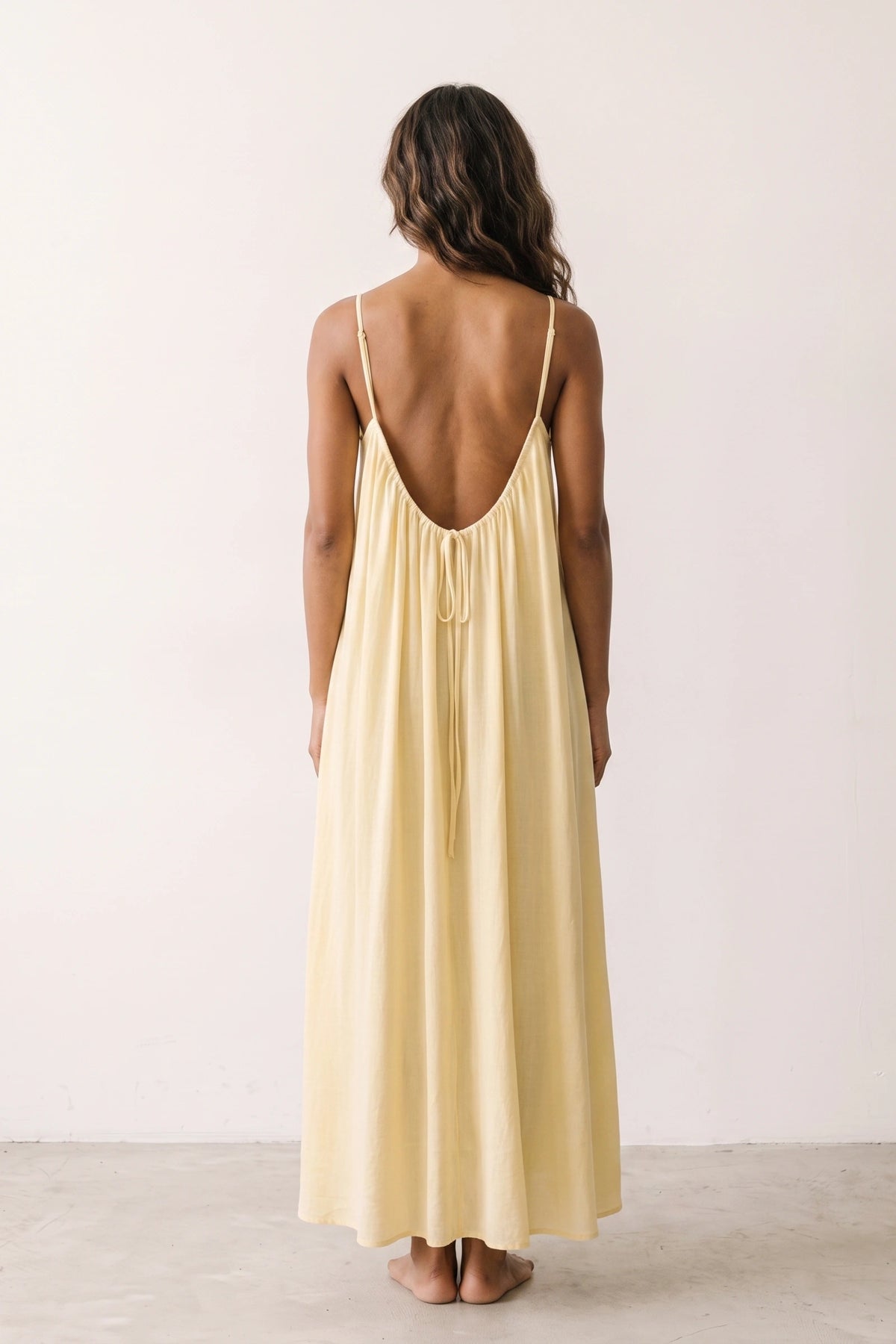 Robe longue casual dos nu Soline couleur Jaune portée de dos par mannequin métisse cheveux détachés, fines bretelles, dos ouvert arrondi avec petit détail bas du dos et coupe fluide sur fond clair