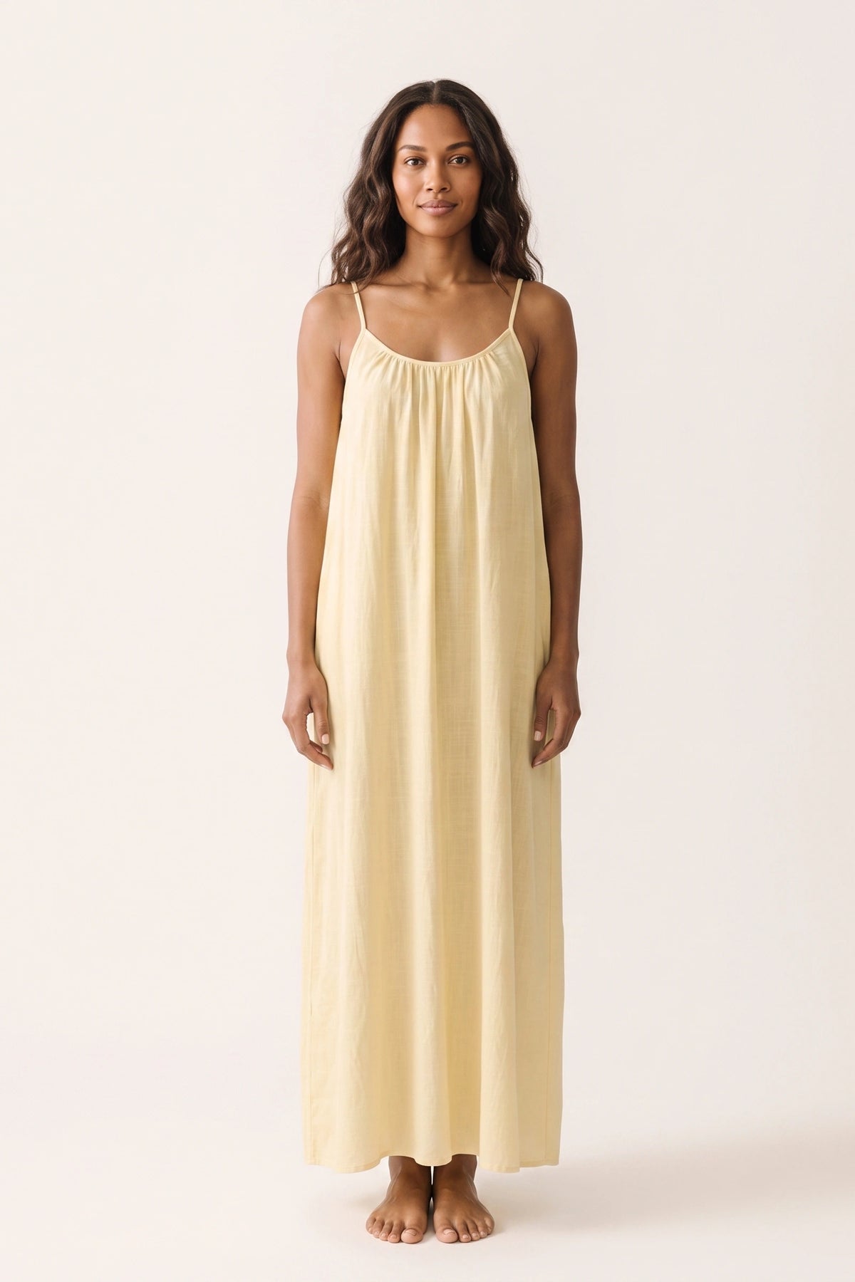 Robe longue casual dos nu Soline couleur Jaune portée de face par mannequin métisse cheveux détachés, fines bretelles, dos ouvert arrondi avec petit détail bas du dos et coupe fluide sur fond clair