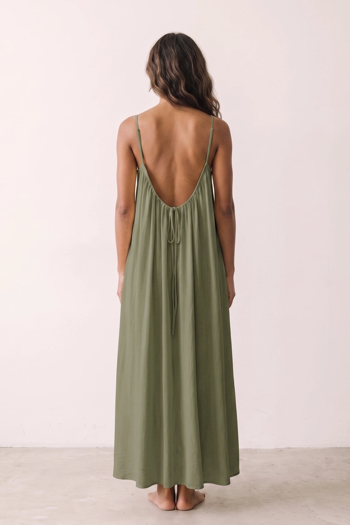 Robe longue casual dos nu Soline couleur Vert portée de dos par mannequin métisse cheveux détachés, fines bretelles, dos ouvert arrondi avec petit détail bas du dos et coupe fluide sur fond clair