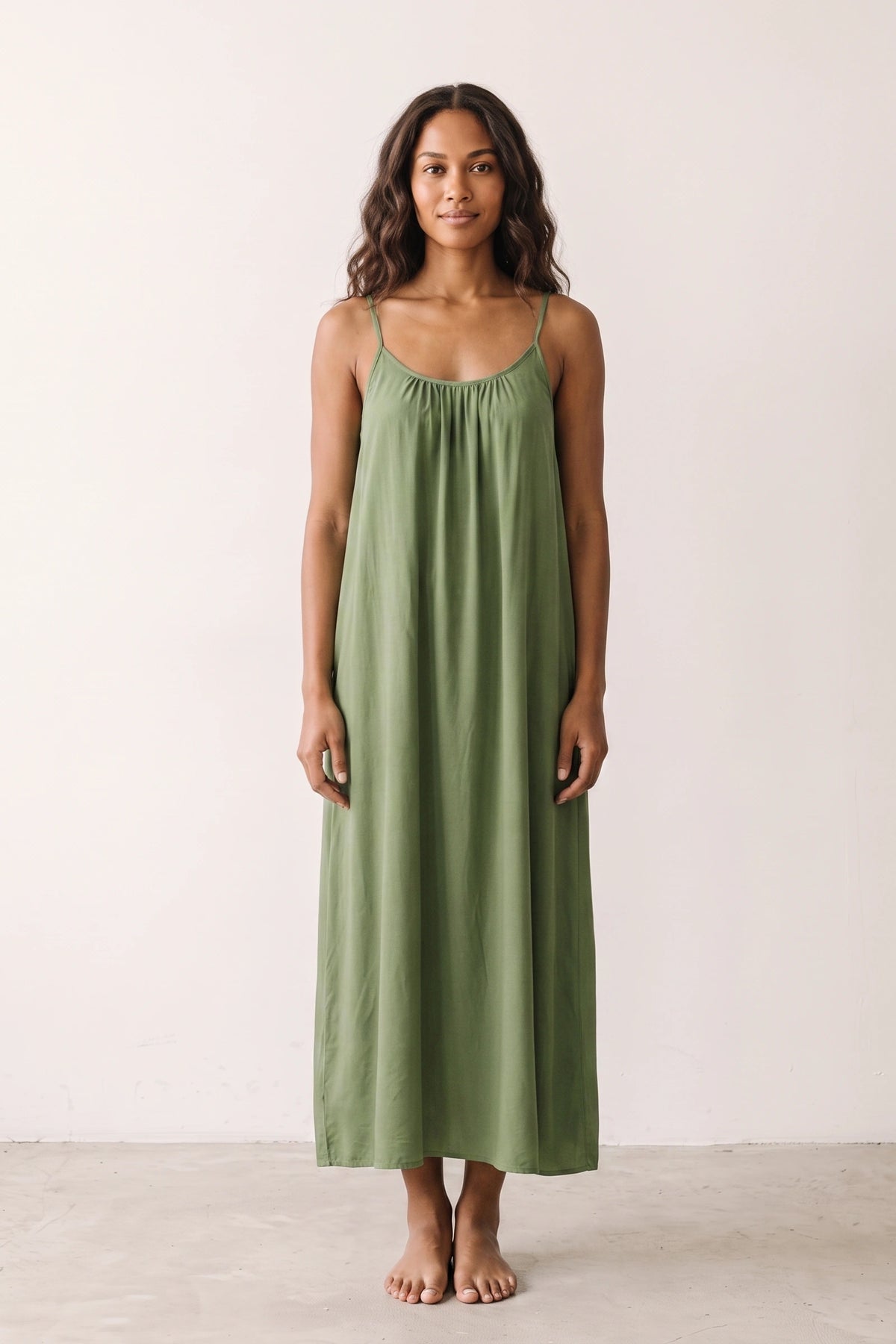 Robe longue casual dos nu Soline couleur Vert portée de face par mannequin métisse cheveux détachés, fines bretelles, dos ouvert arrondi avec petit détail bas du dos et coupe fluide sur fond clair