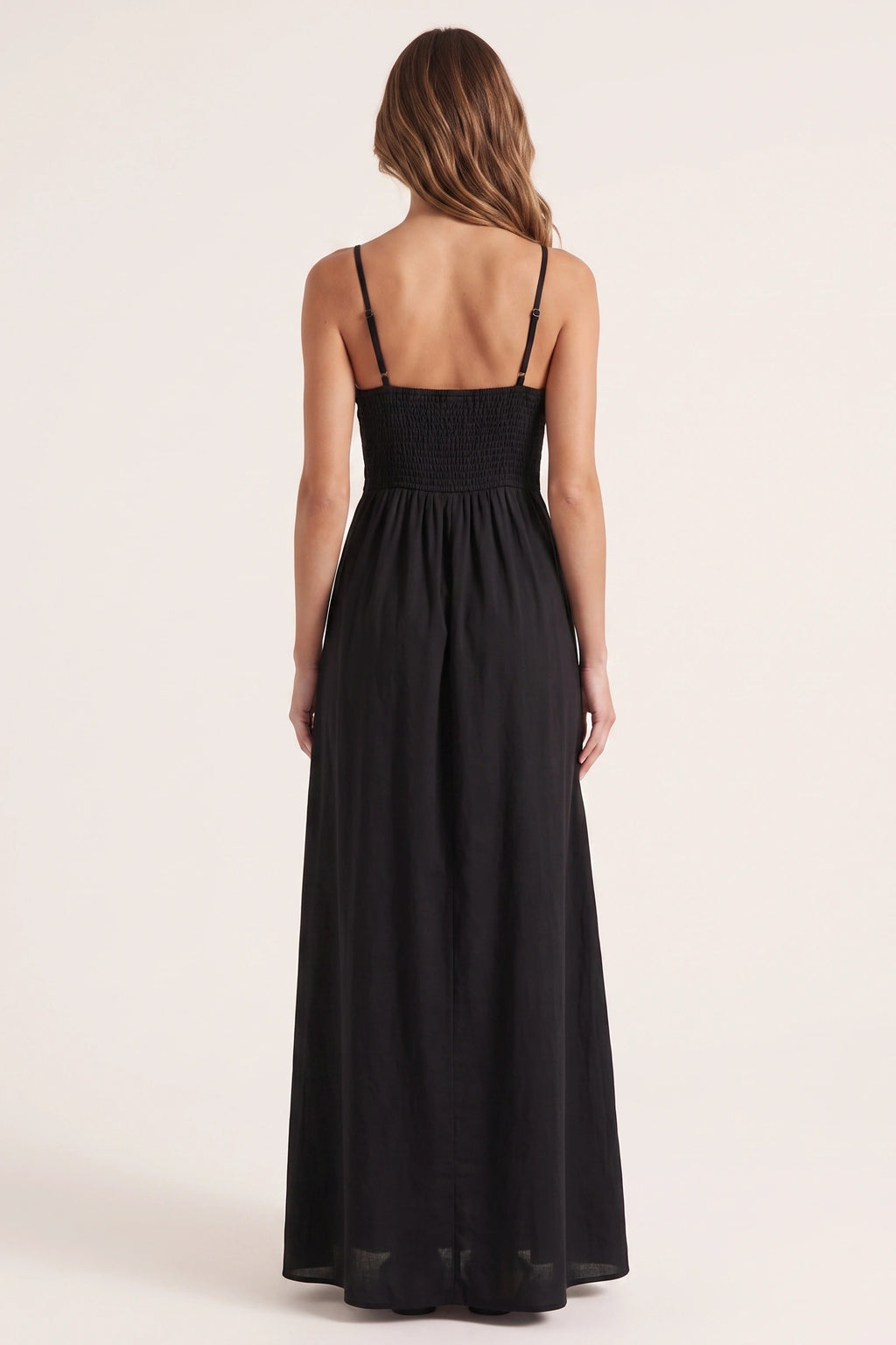 Robe longue casual noire Ava portée de dos par Élena cheveux détachés, dos smocké, fines bretelles et jupe longue fluide sur fond neutre