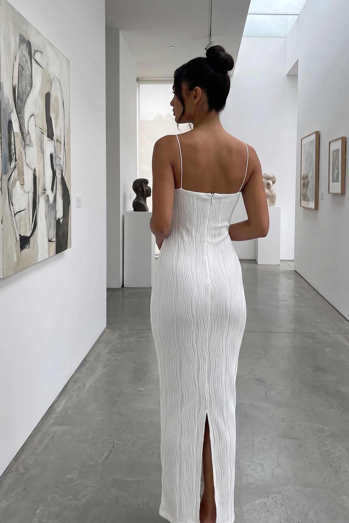 Robe moulante longue Maëlys blanche portée de dos par Diane Camille dans une galerie moderne, haut du dos droit fidèle fournisseur, fines bretelles et fente arrière