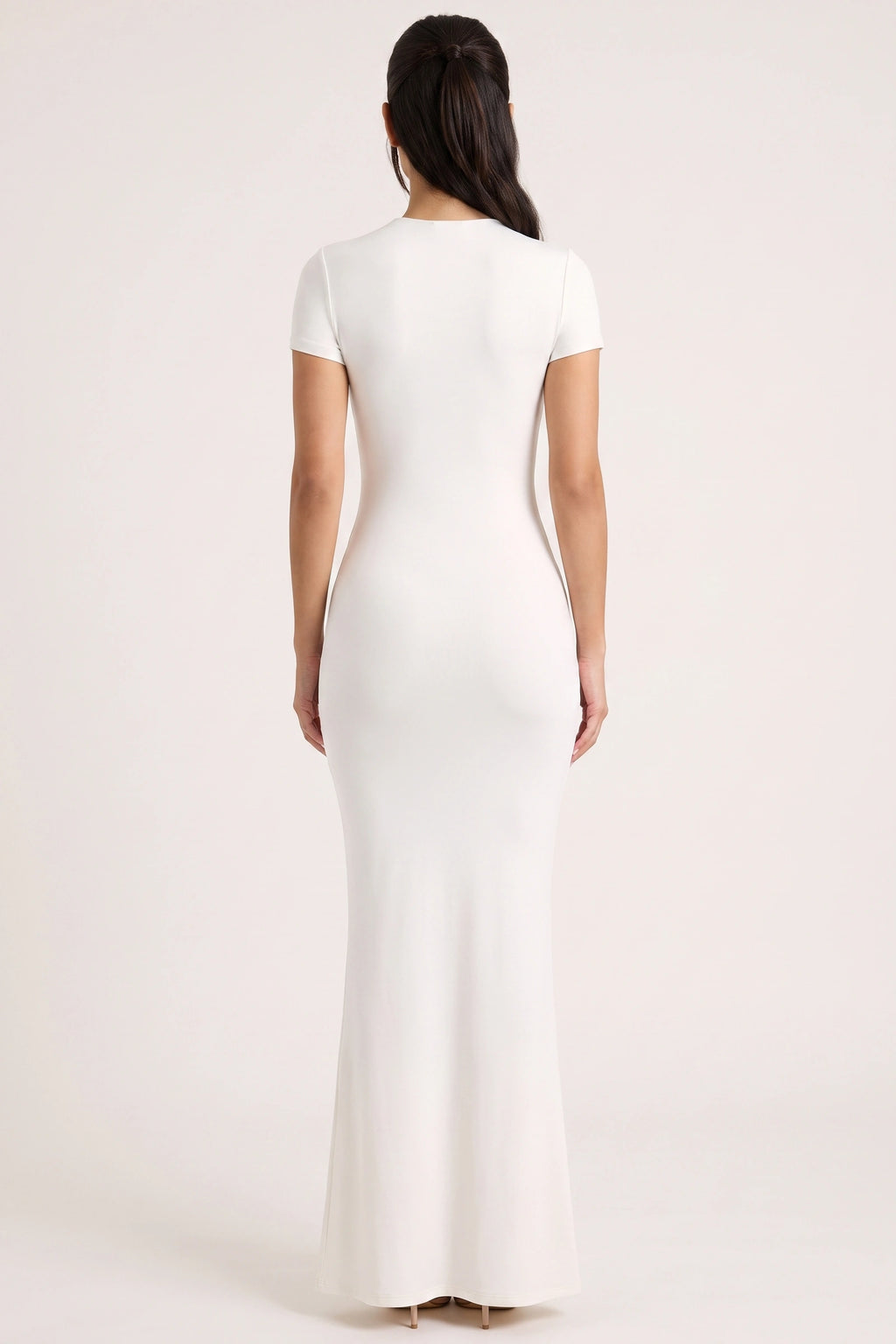Robe moulante longue Mila blanche portée de dos par Camille sur fond neutre clair, dos uni et coupe longue ajustée