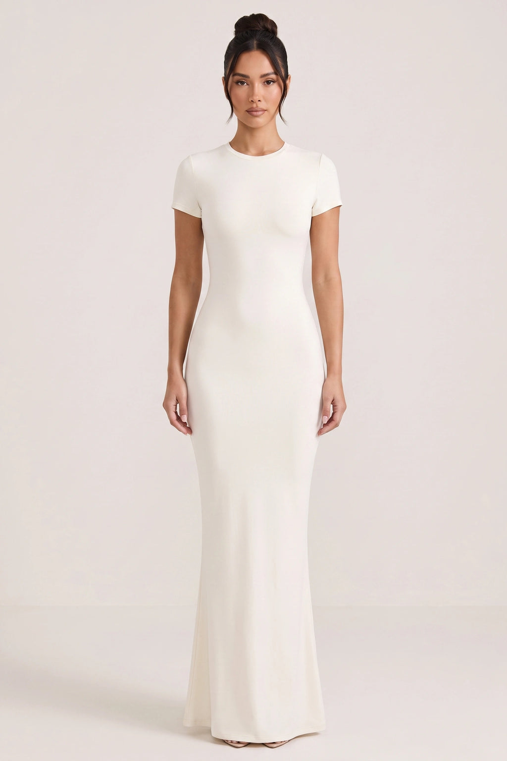 Robe moulante longue Mila blanche portée de face par Camille sur fond neutre clair, col rond, manches courtes et silhouette ajustée