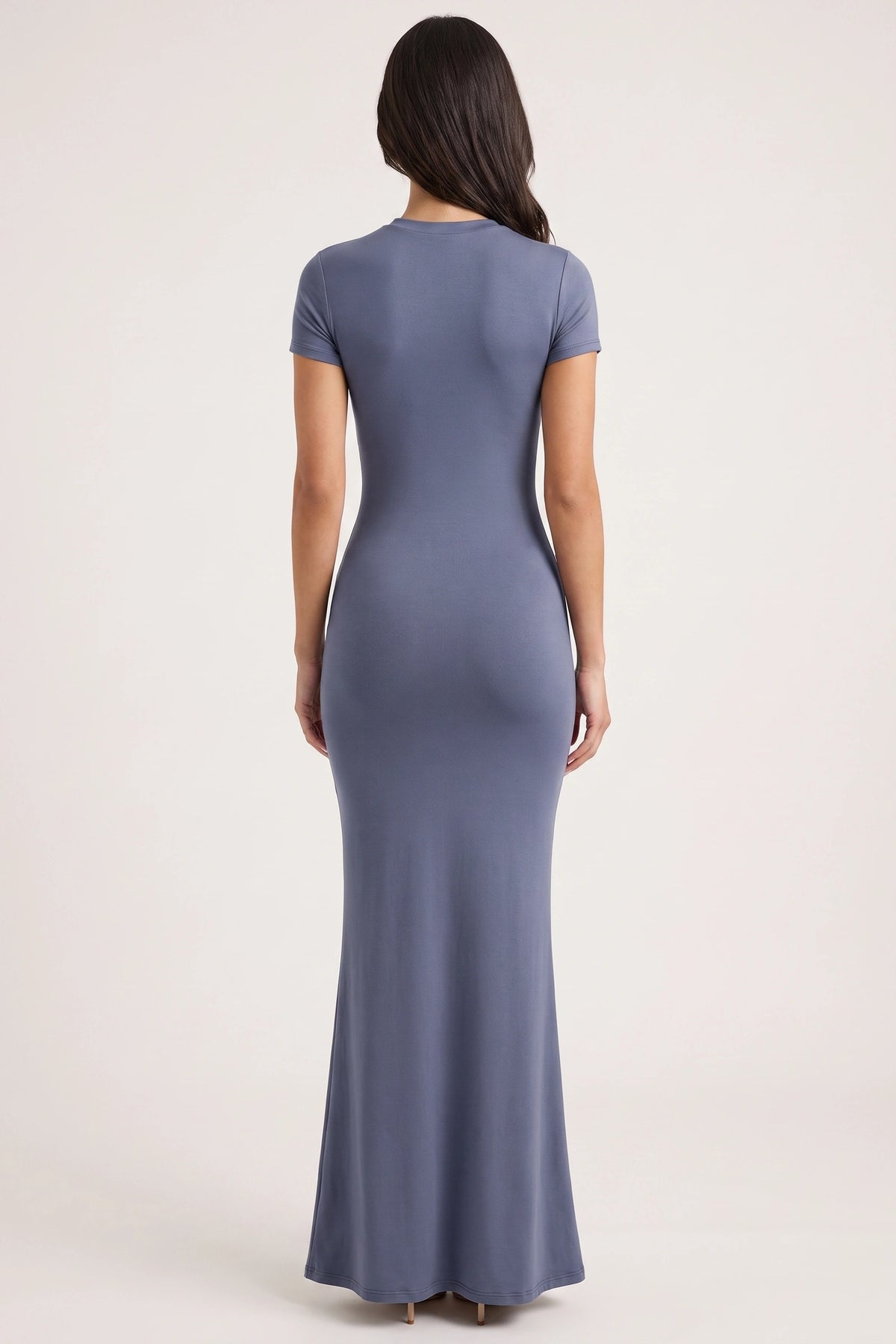 Robe moulante longue Mila bleu grisé portée de dos par Camille sur fond neutre clair, dos simple et longueur cheville
