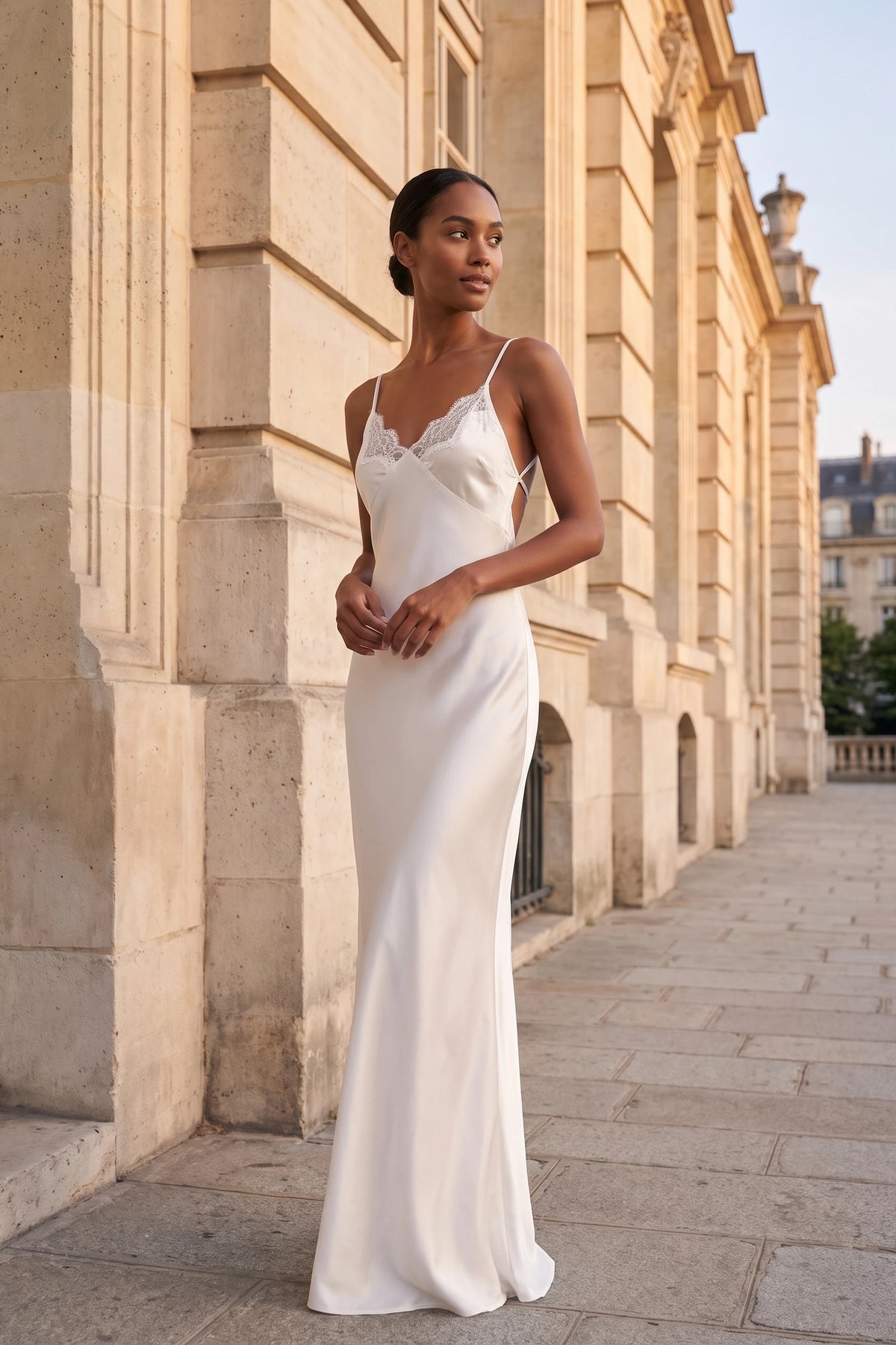 Robe satin dentelle dos nu Alyssa blanche portée par une mannequin métisse devant une façade élégante, allure cérémonie chic sans alcool